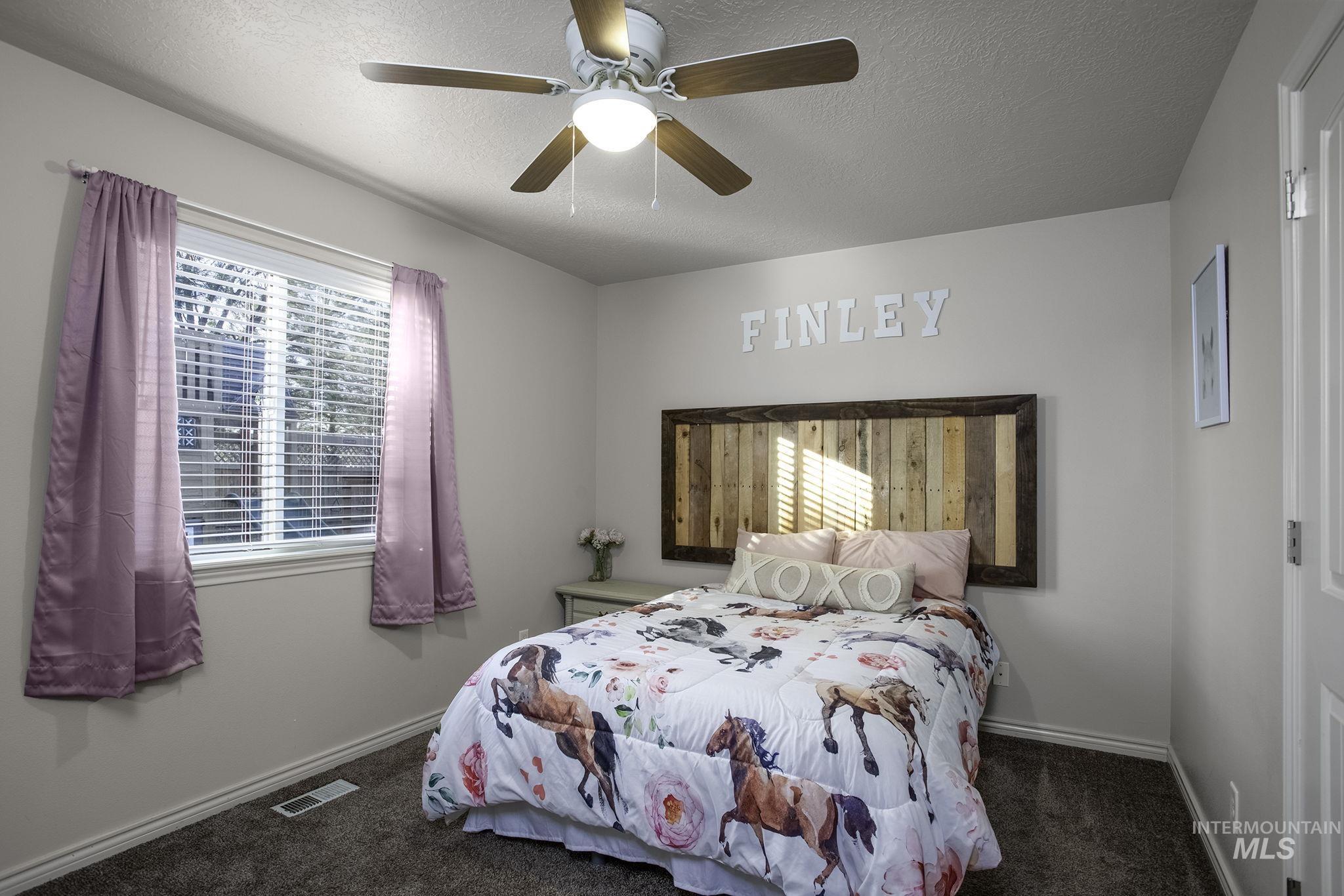 Bedroom featuring a ceiling fan, multiple windows, dark colored carpet, and a textured ceiling