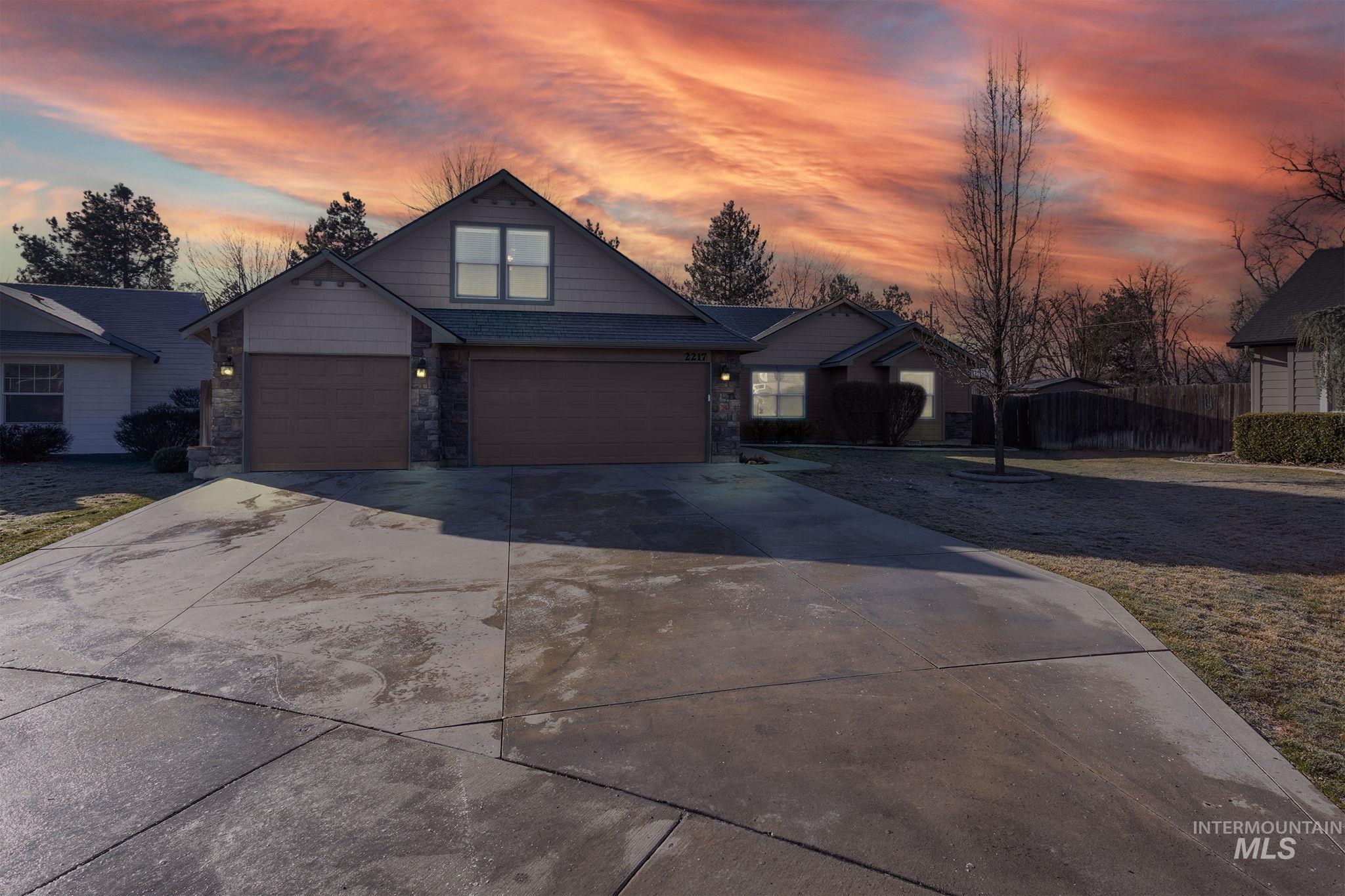 View of front facade with driveway, stone siding, and an attached garage