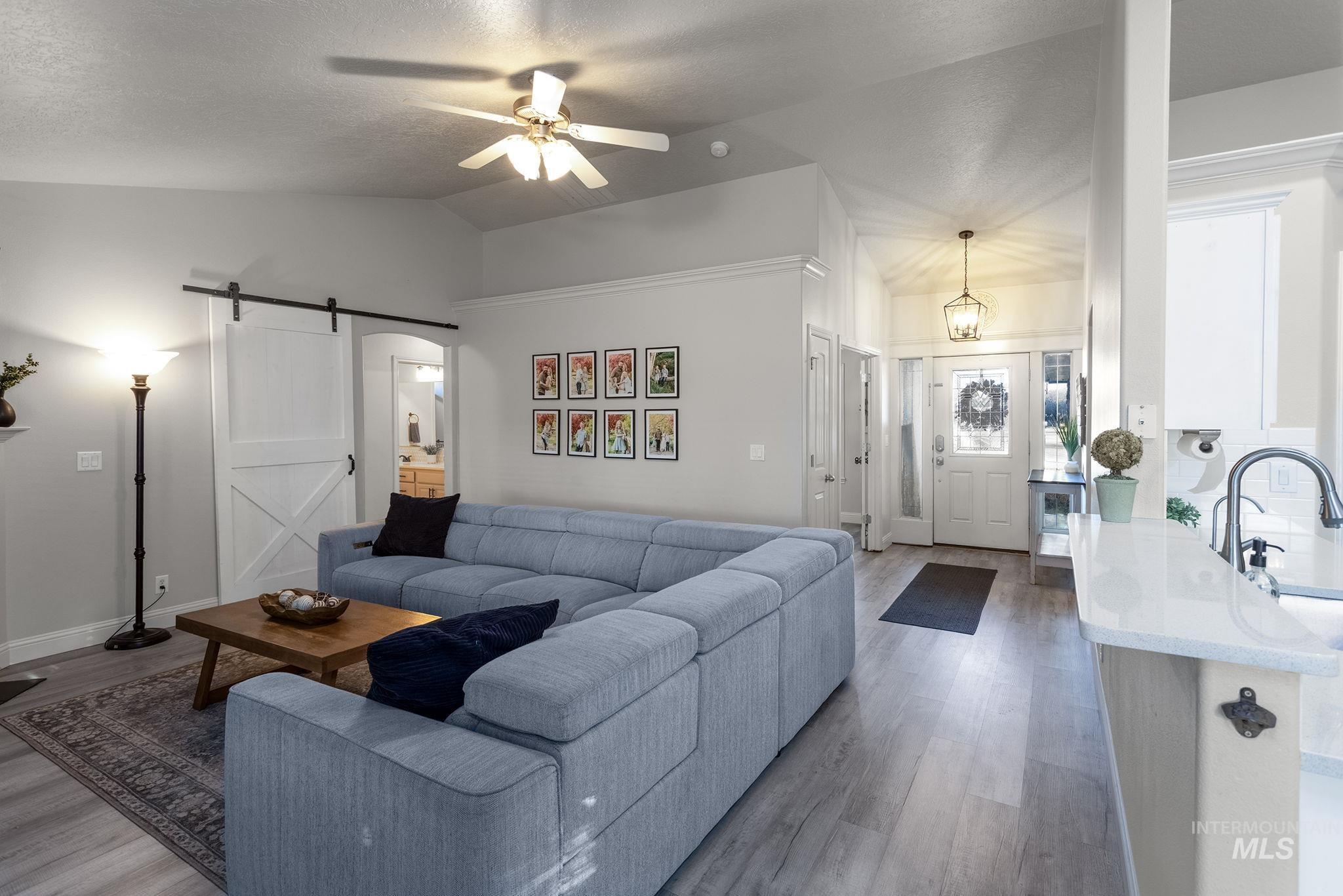 Living area with a barn door, light wood-type flooring, ceiling fan, lofted ceiling, and a textured ceiling