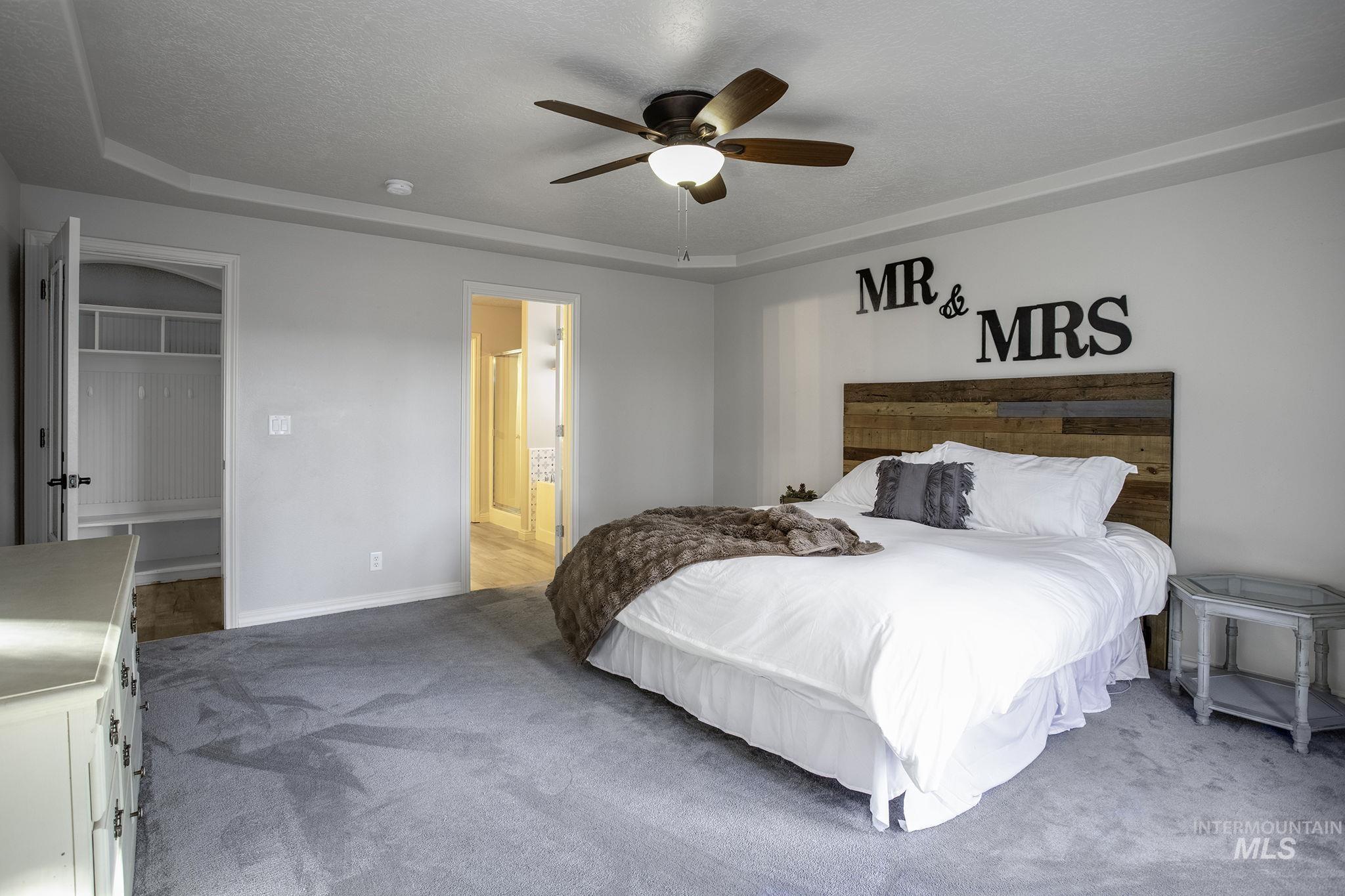 Carpeted bedroom featuring a tray ceiling, ceiling fan, ensuite bath, and a textured ceiling
