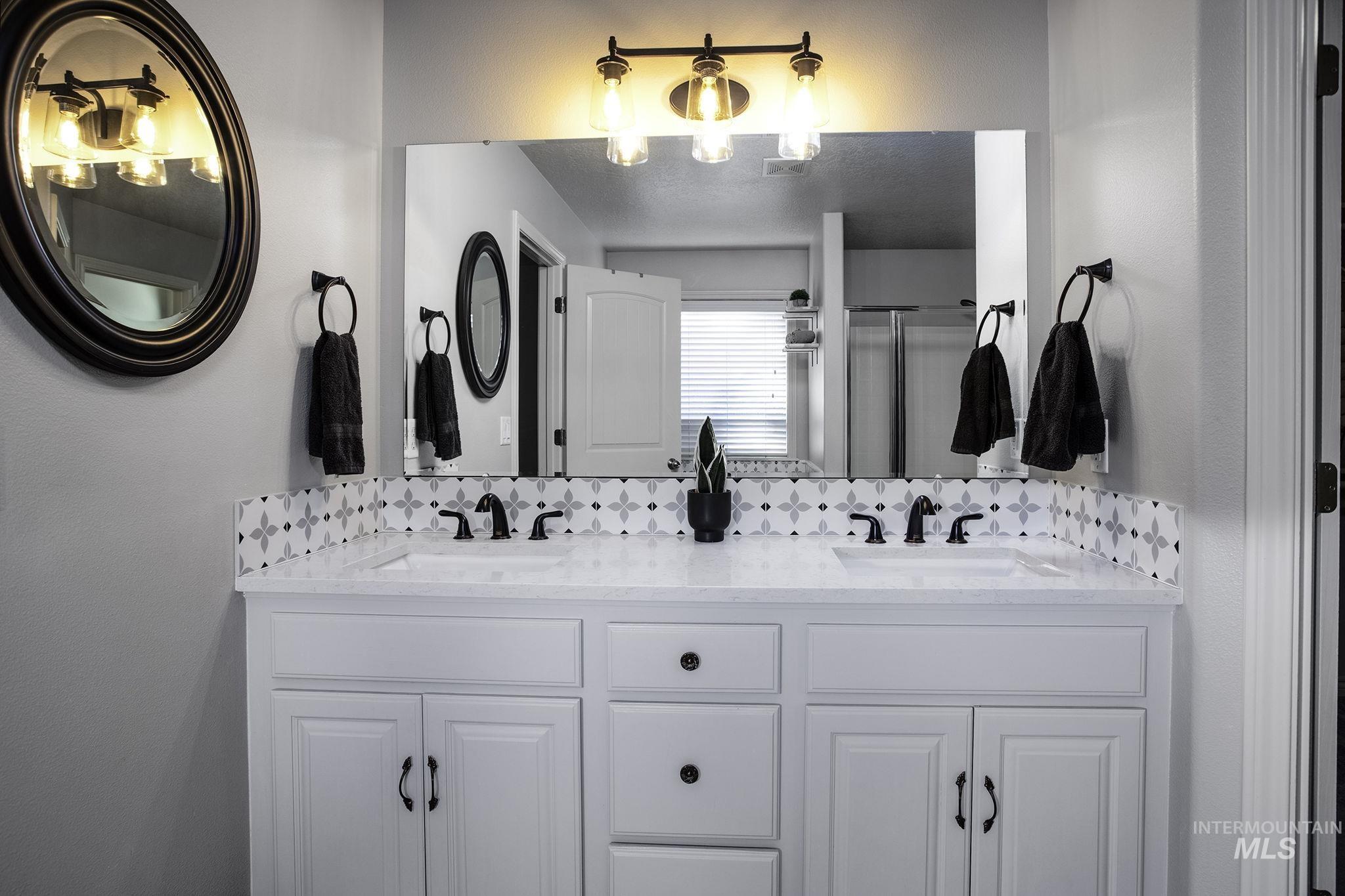 Bathroom featuring double vanity, decorative backsplash, and a shower stall