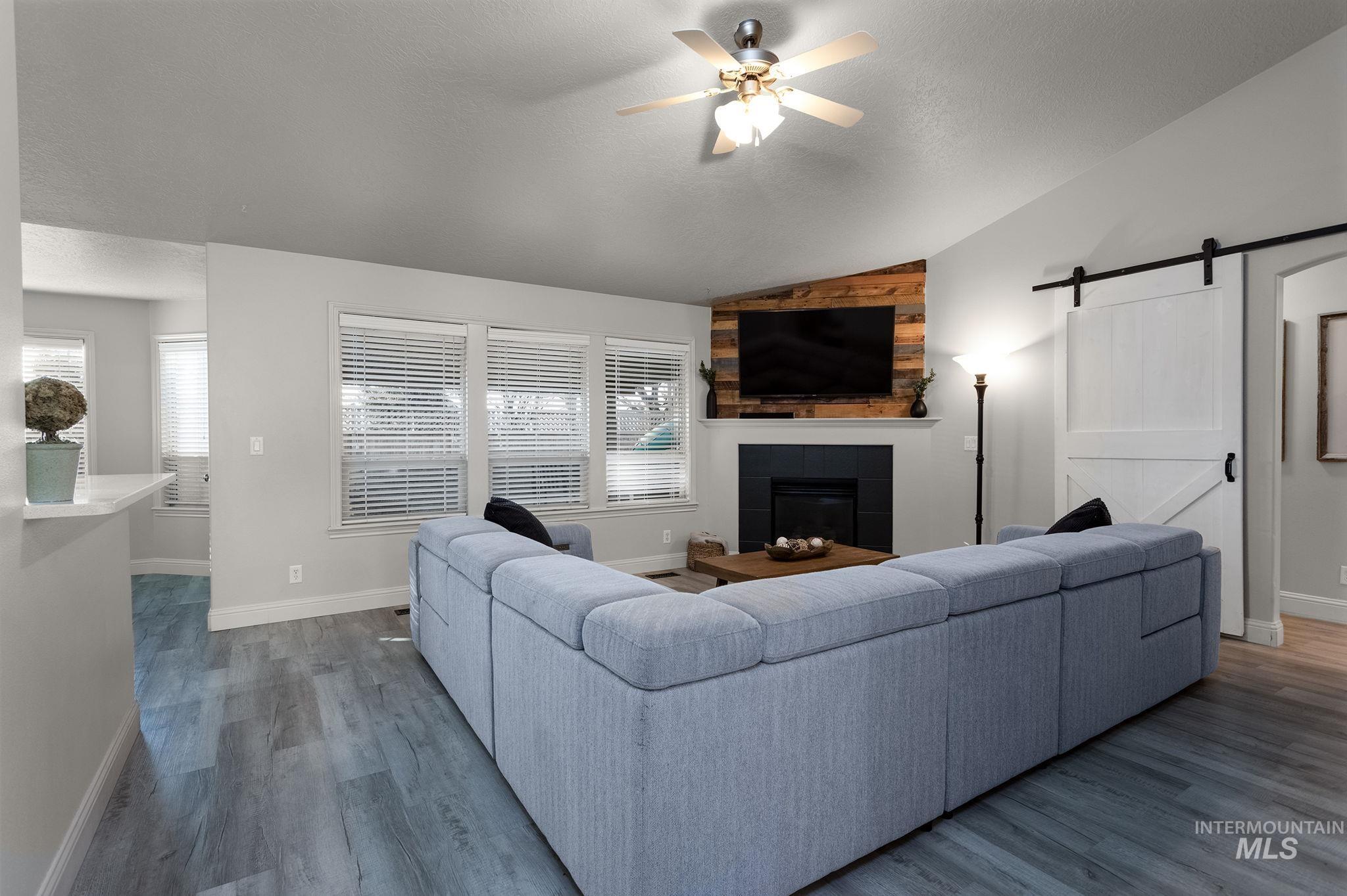 Living area featuring a barn door, lofted ceiling, a ceiling fan, dark wood-style flooring, and a tiled fireplace