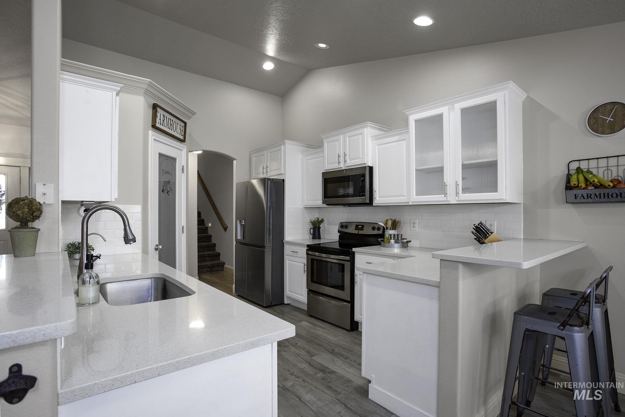 Kitchen featuring light stone counters, white cabinetry, stainless steel appliances, glass insert cabinets, and a peninsula