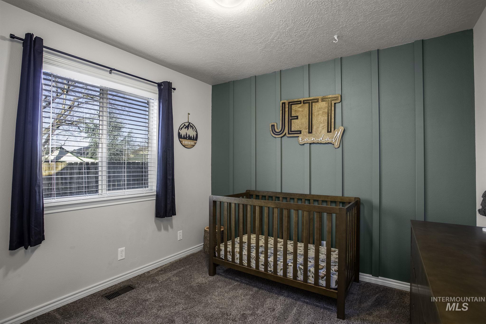 Bedroom featuring a decorative wall, a crib, dark colored carpet, and a textured ceiling