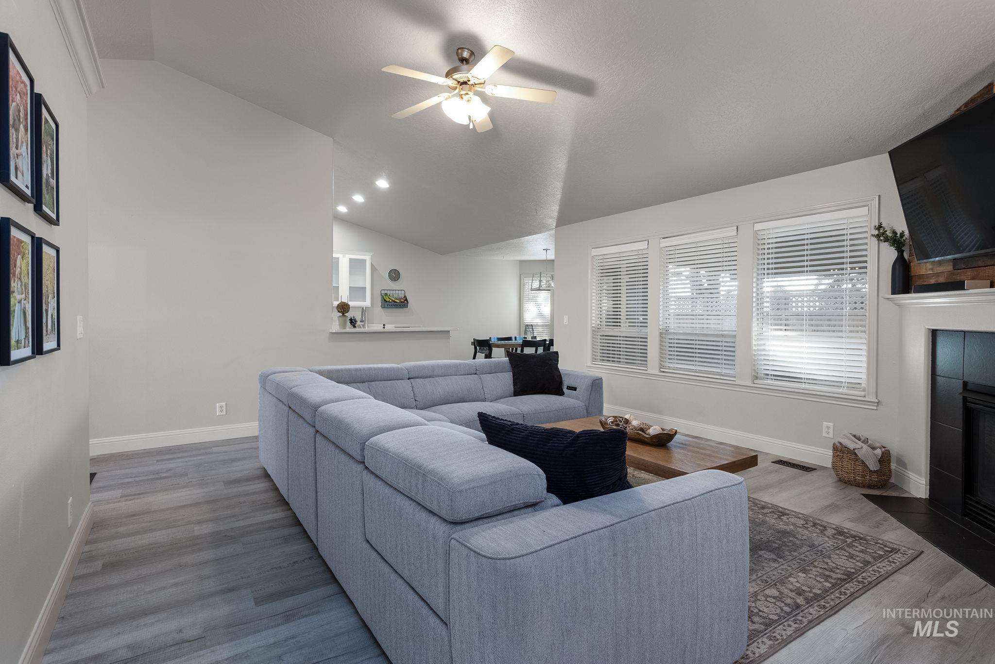 Living room with vaulted ceiling, a fireplace, wood finished floors, and a ceiling fan