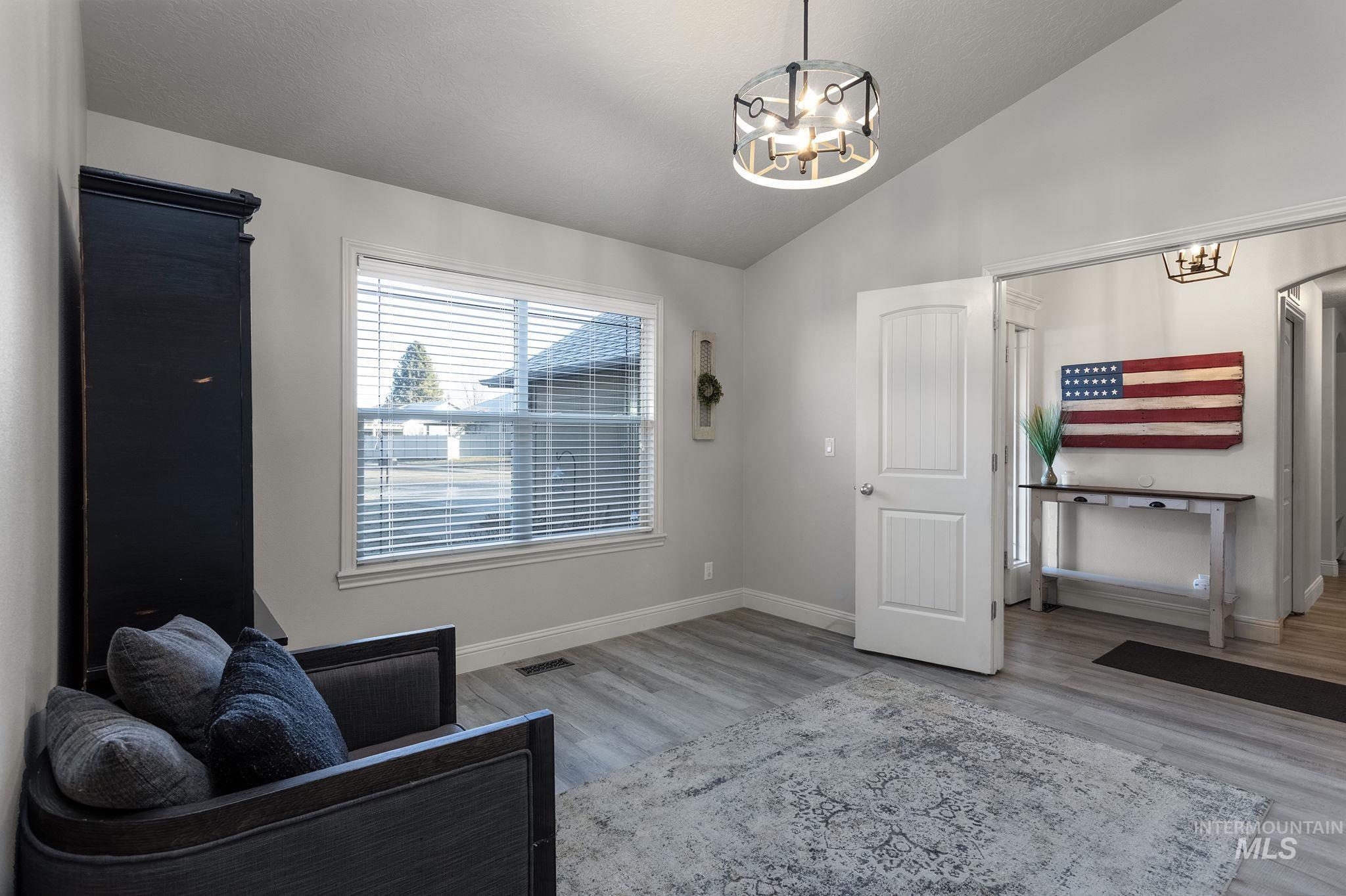 Living area featuring light wood-style flooring, vaulted ceiling, and a chandelier