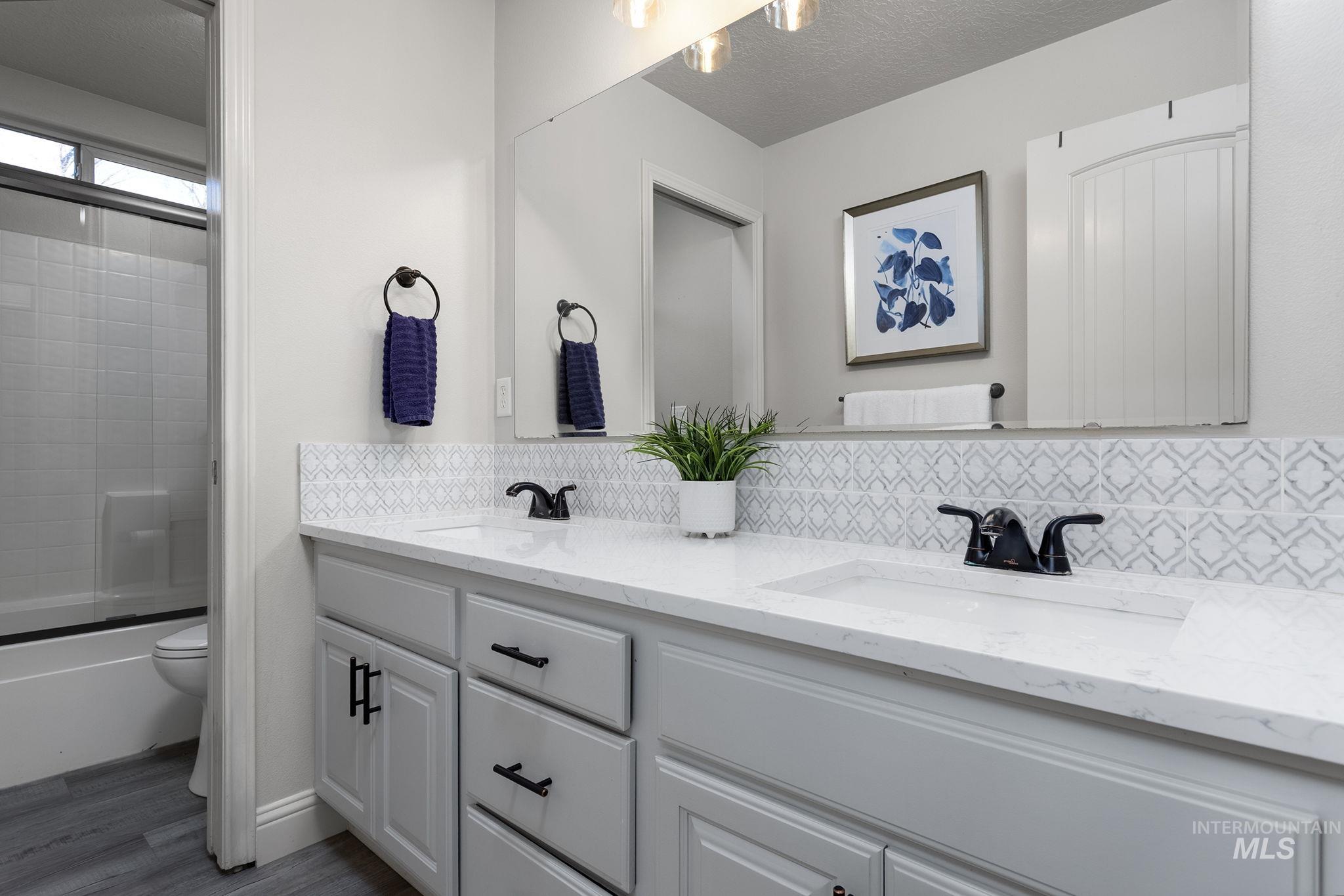 Full bathroom featuring double vanity, bath / shower combo with glass door, tasteful backsplash, and a textured ceiling