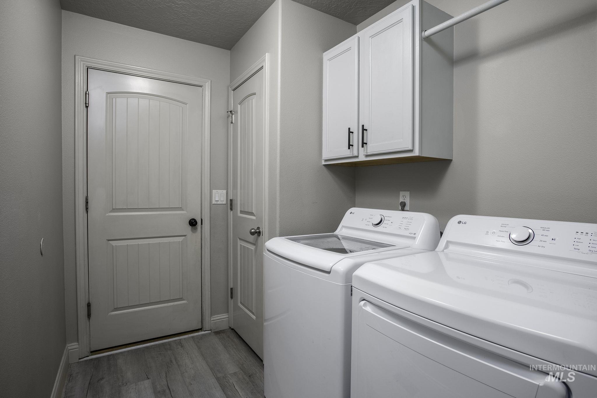 Laundry area featuring separate washer and dryer, cabinet space, light wood finished floors, and a textured ceiling