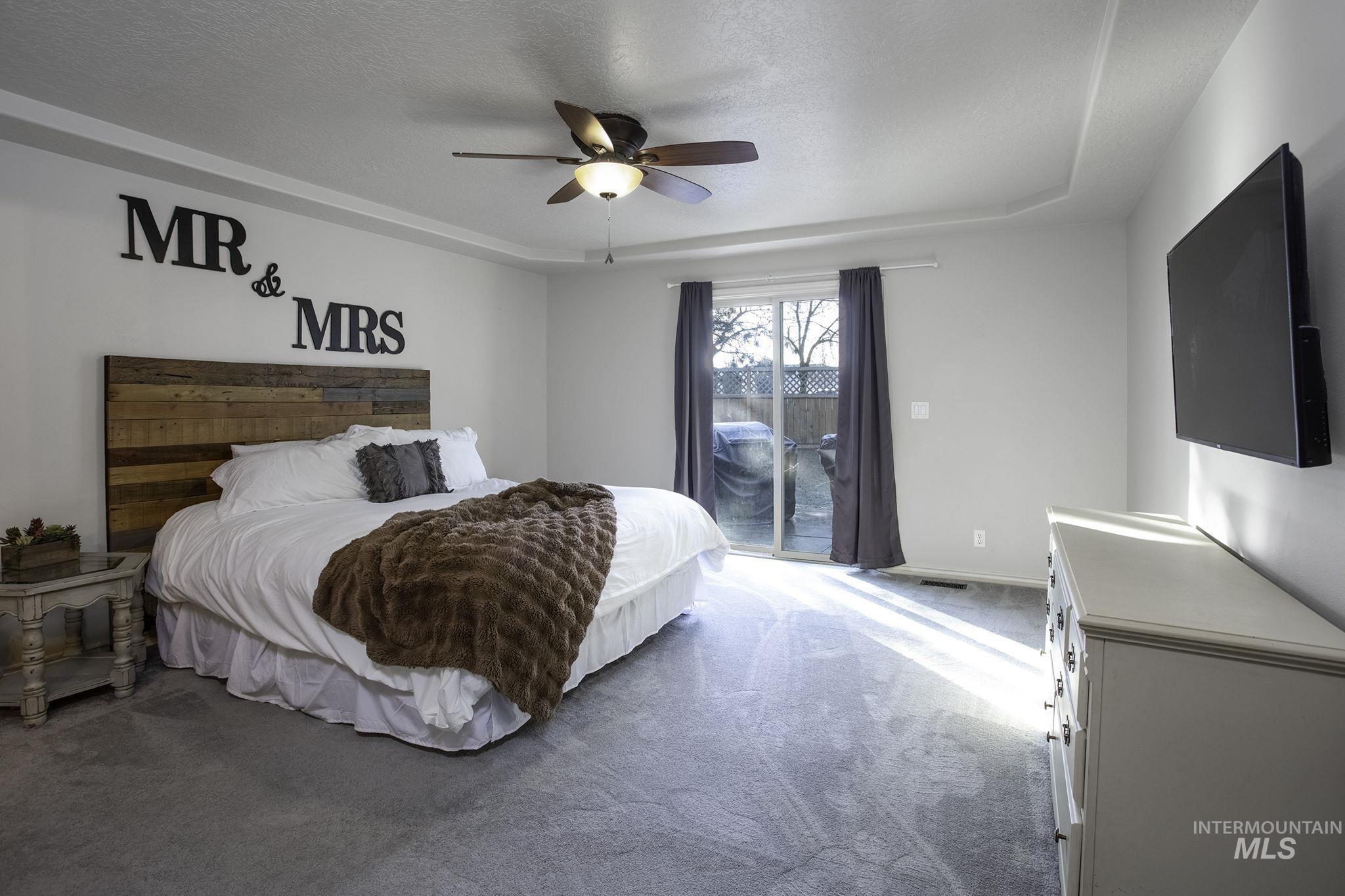 Carpeted bedroom with access to outside, a ceiling fan, a textured ceiling, and a raised ceiling