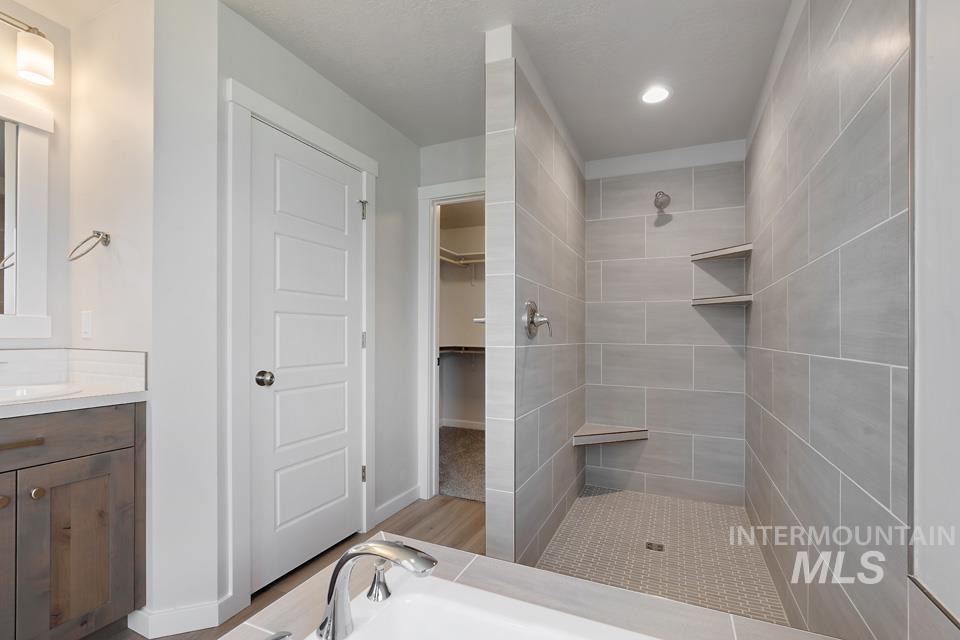 Full bathroom featuring tiled shower, vanity, and a walk in closet