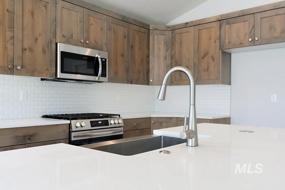 Kitchen with stainless steel appliances, tasteful backsplash, light countertops, and vaulted ceiling