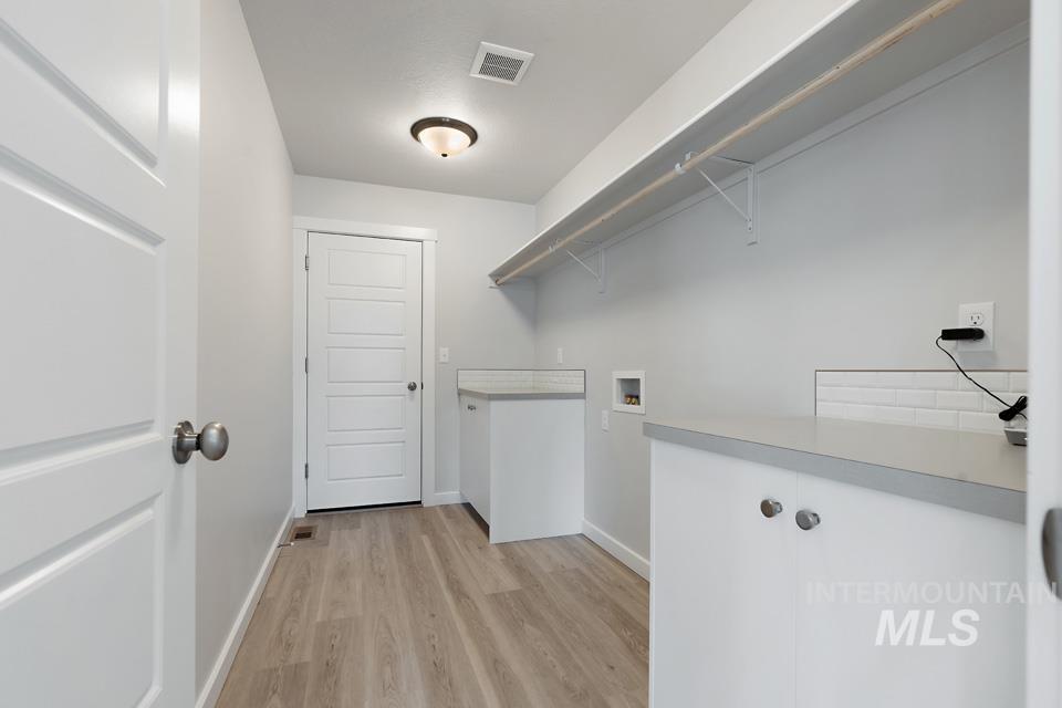 Washroom featuring light wood-type flooring, washer hookup, and cabinet space