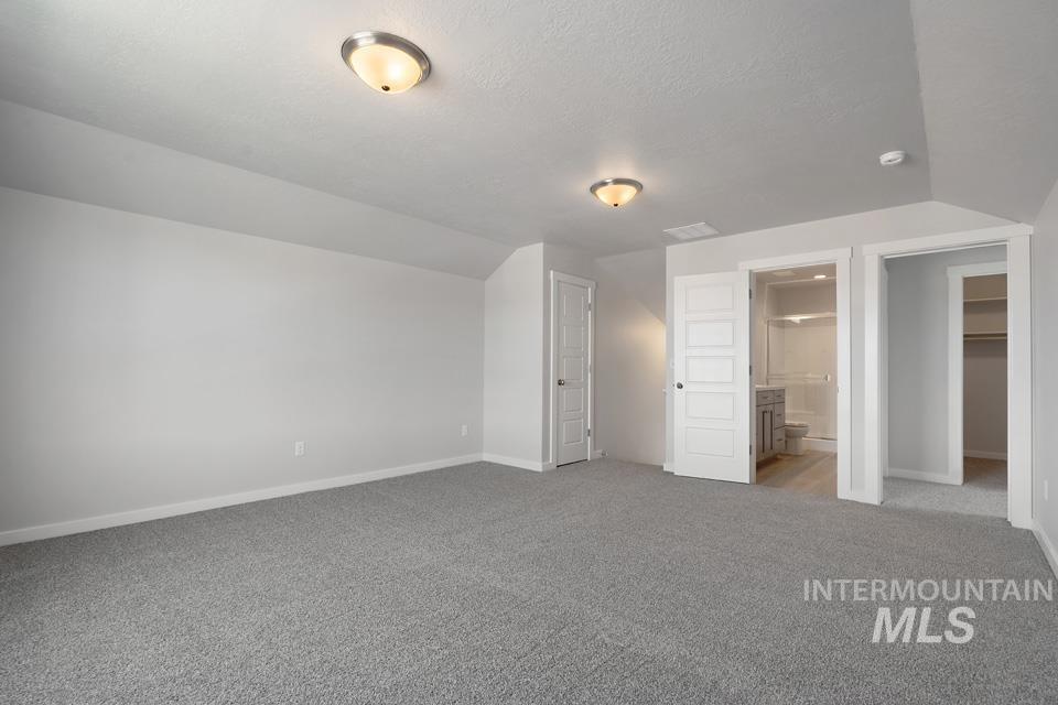 Unfurnished bedroom with carpet, vaulted ceiling, connected bathroom, and a textured ceiling
