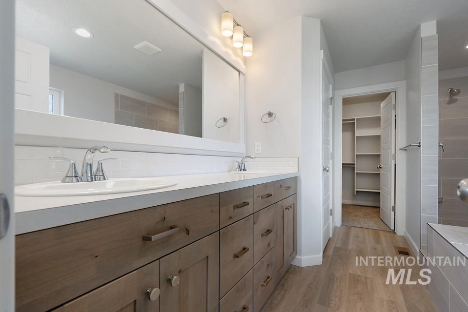 Bathroom with double vanity, wood finished floors, recessed lighting, tiled shower, and a walk in closet