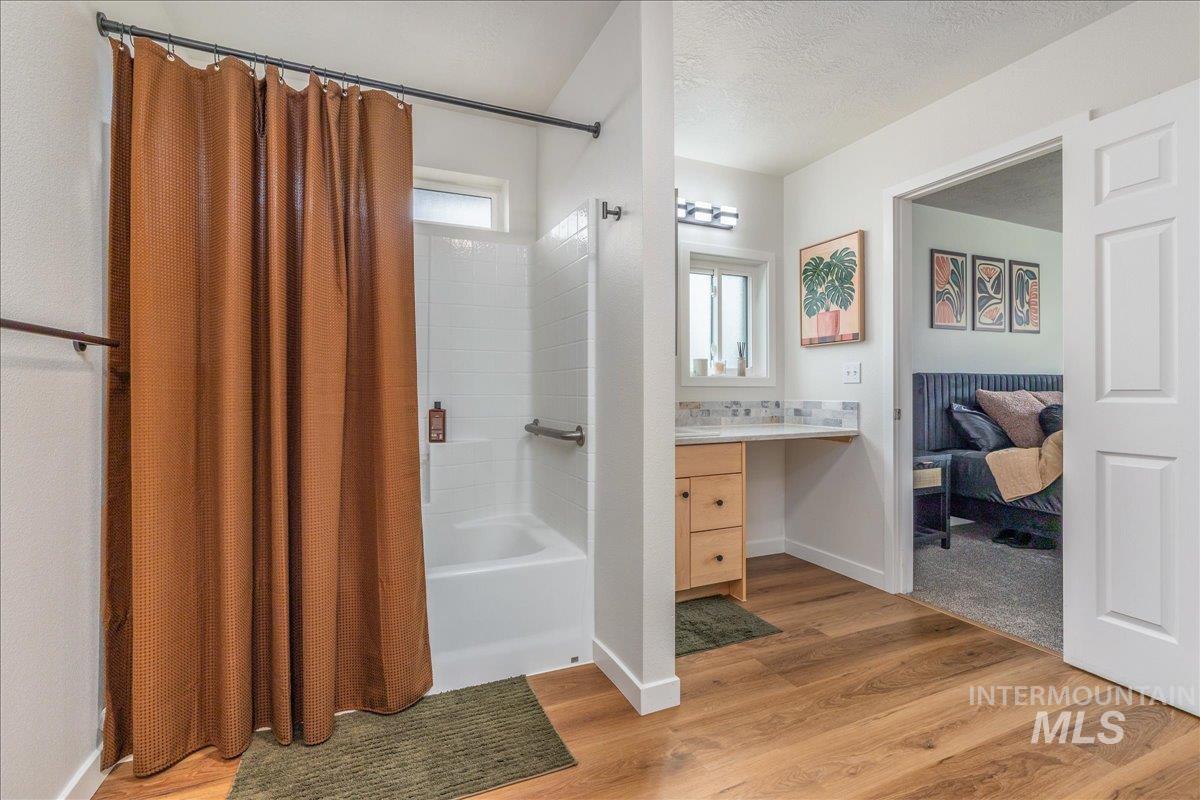 Ensuite bathroom featuring vanity, shower / bath combo, light wood-type flooring, and a textured ceiling