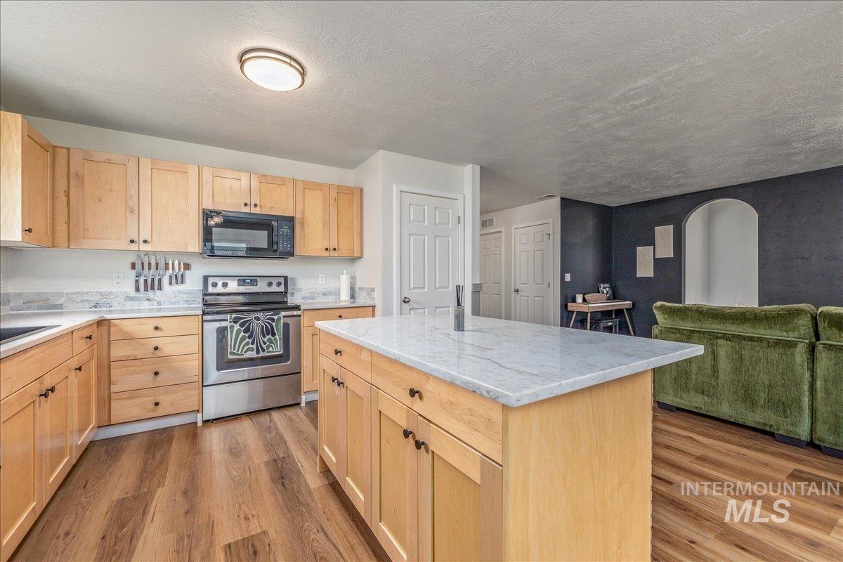 Kitchen featuring light wood finish cabinets, stainless steel electric range, a kitchen island, black microwave, and light wood-style flooring