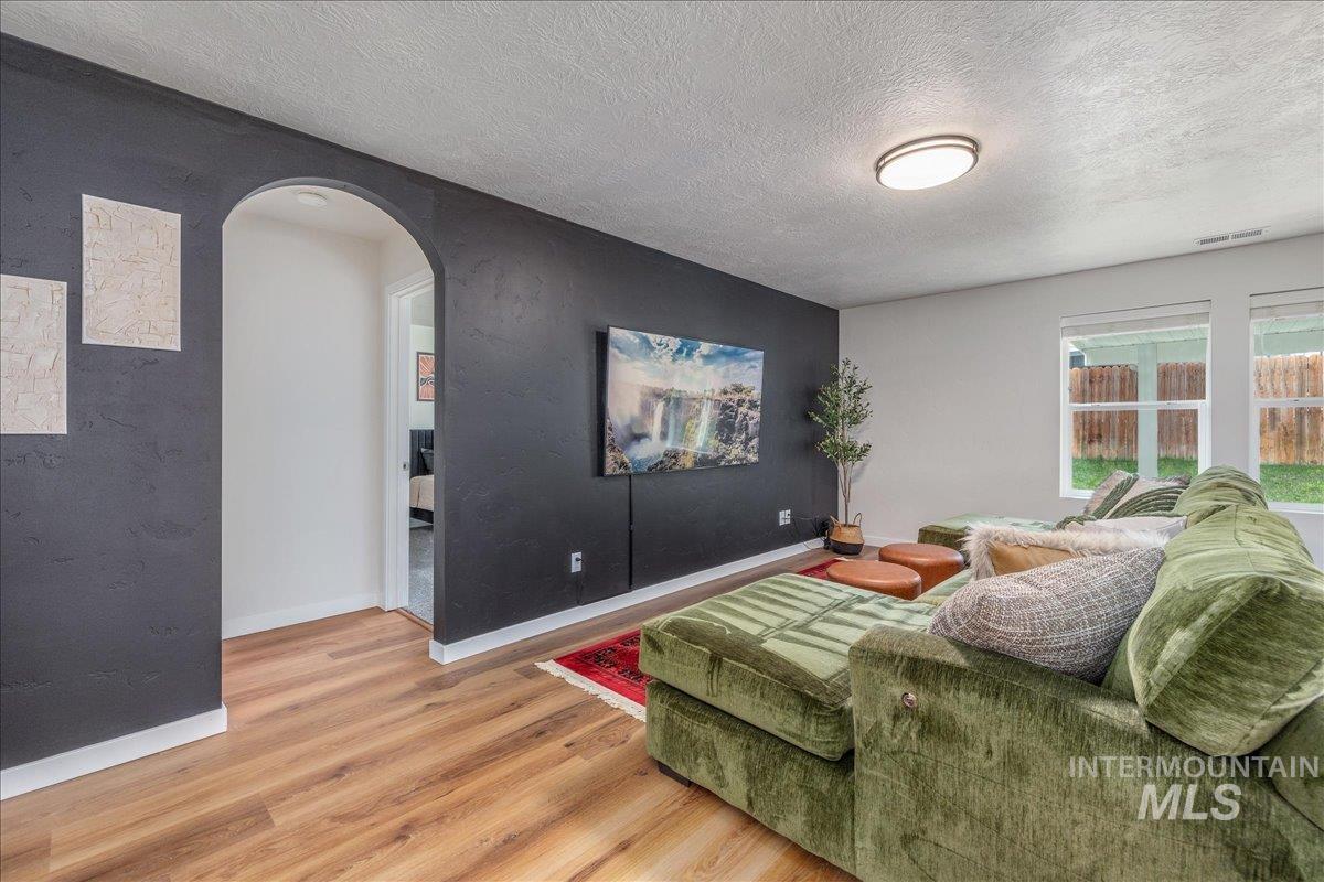 Living area featuring arched walkways, light wood-style flooring, and a textured ceiling