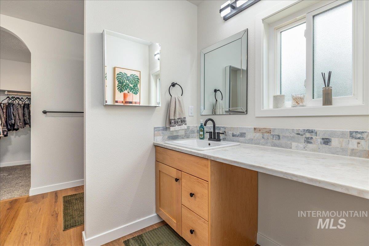 Full bath with vanity, a spacious closet, and light wood-style flooring