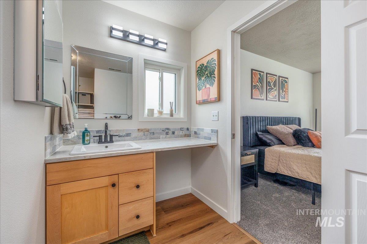 Ensuite bathroom with vanity, light wood-style flooring, and a textured ceiling