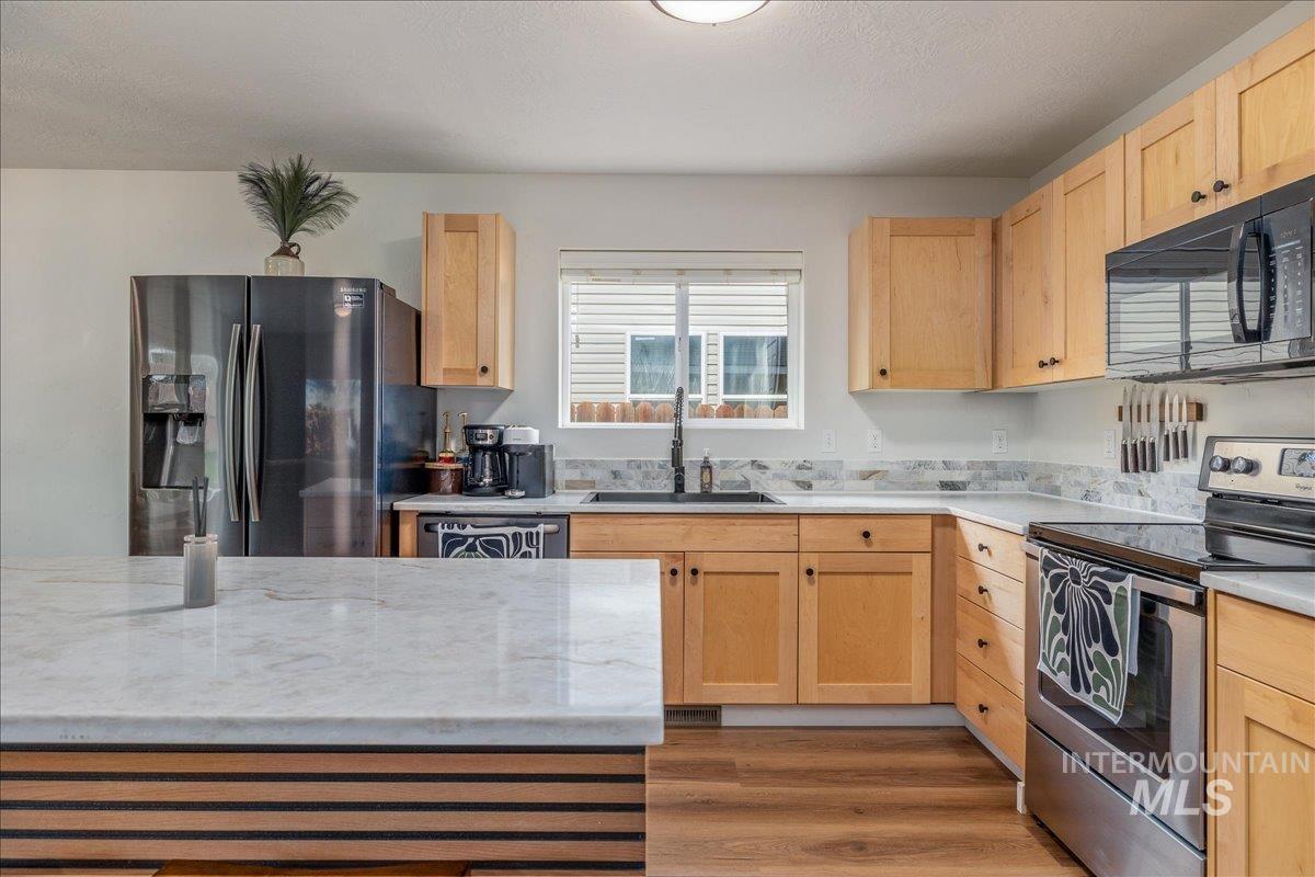 Kitchen with stainless steel appliances, light wood finish cabinetry, light stone counters, wood finished floors, and a textured ceiling