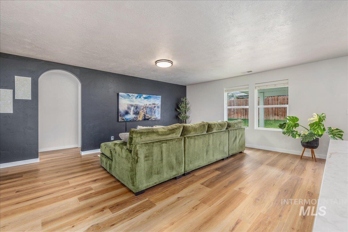 Living area featuring arched walkways, light wood-style floors, and a textured ceiling