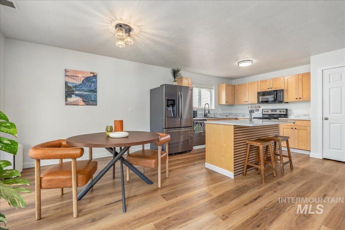 Kitchen with stainless steel appliances, a center island with sink, light wood finish cabinets, light wood-style flooring, and a textured ceiling