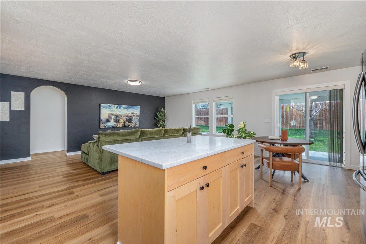 Kitchen featuring light wood finish cabinetry, a kitchen island, light wood finished floors, arched walkways, and a textured ceiling