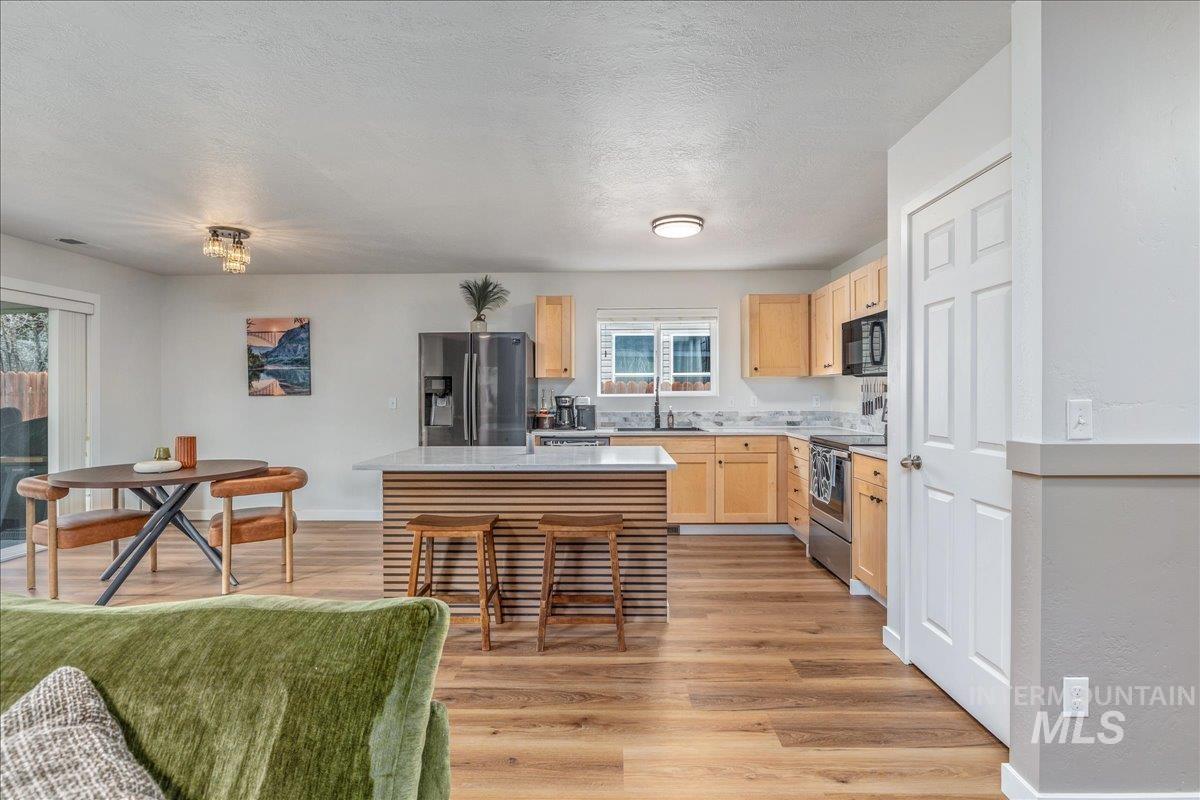 Kitchen with light wood finish cabinets, a kitchen island, stainless steel appliances, light wood-style floors, and a kitchen breakfast bar