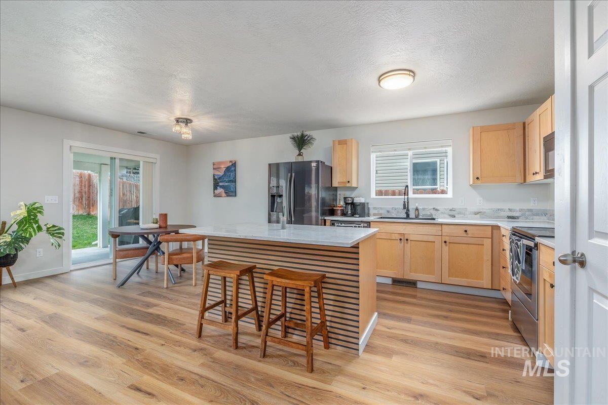 Kitchen with light wood finish cabinets, a center island, stainless steel appliances, a kitchen breakfast bar, and light wood-style flooring