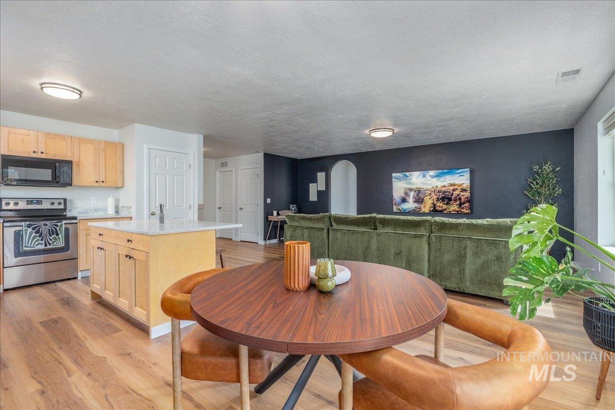 Dining space with light wood-type flooring, arched walkways, and a textured ceiling