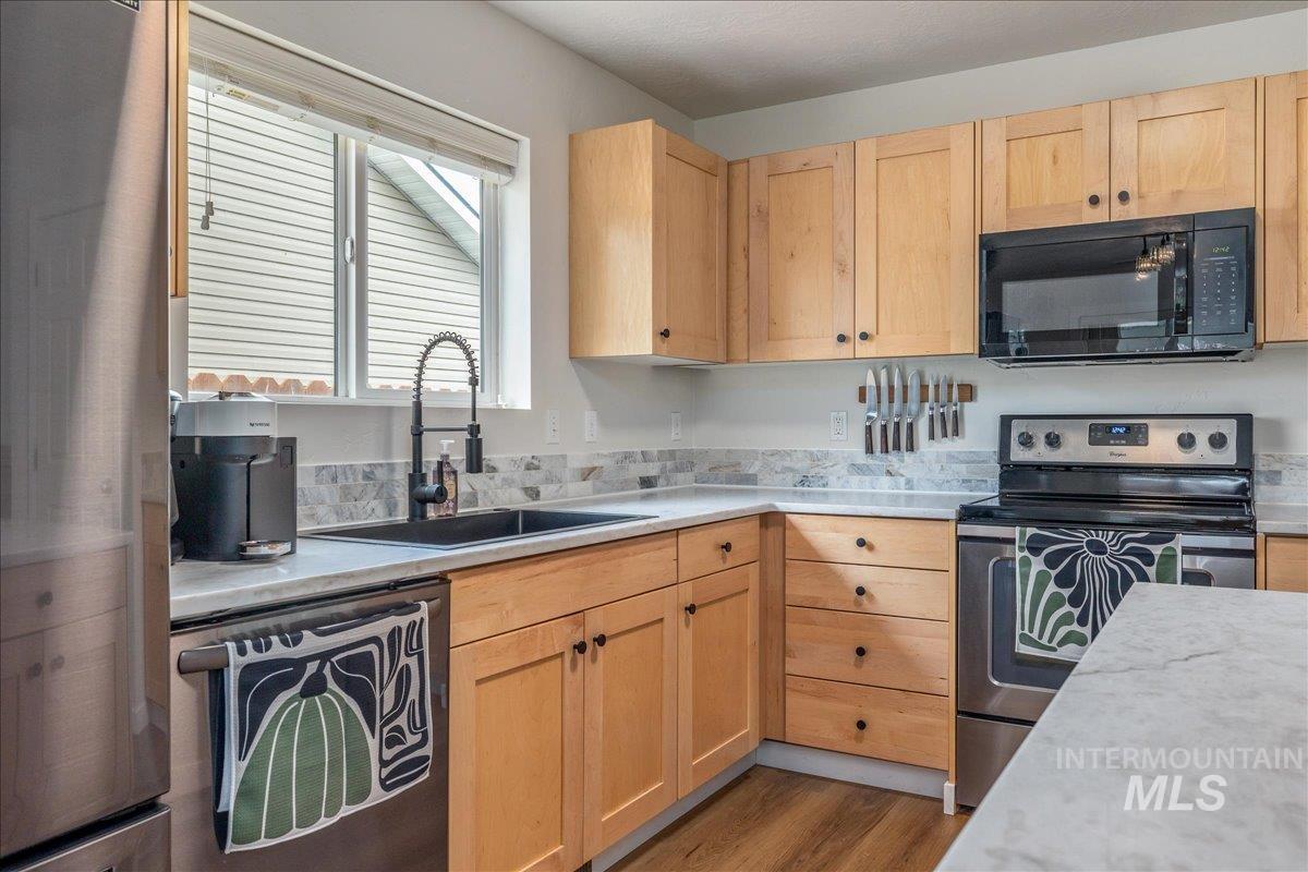 Kitchen featuring stainless steel appliances, light wood finish cabinetry, and dark wood finished floors