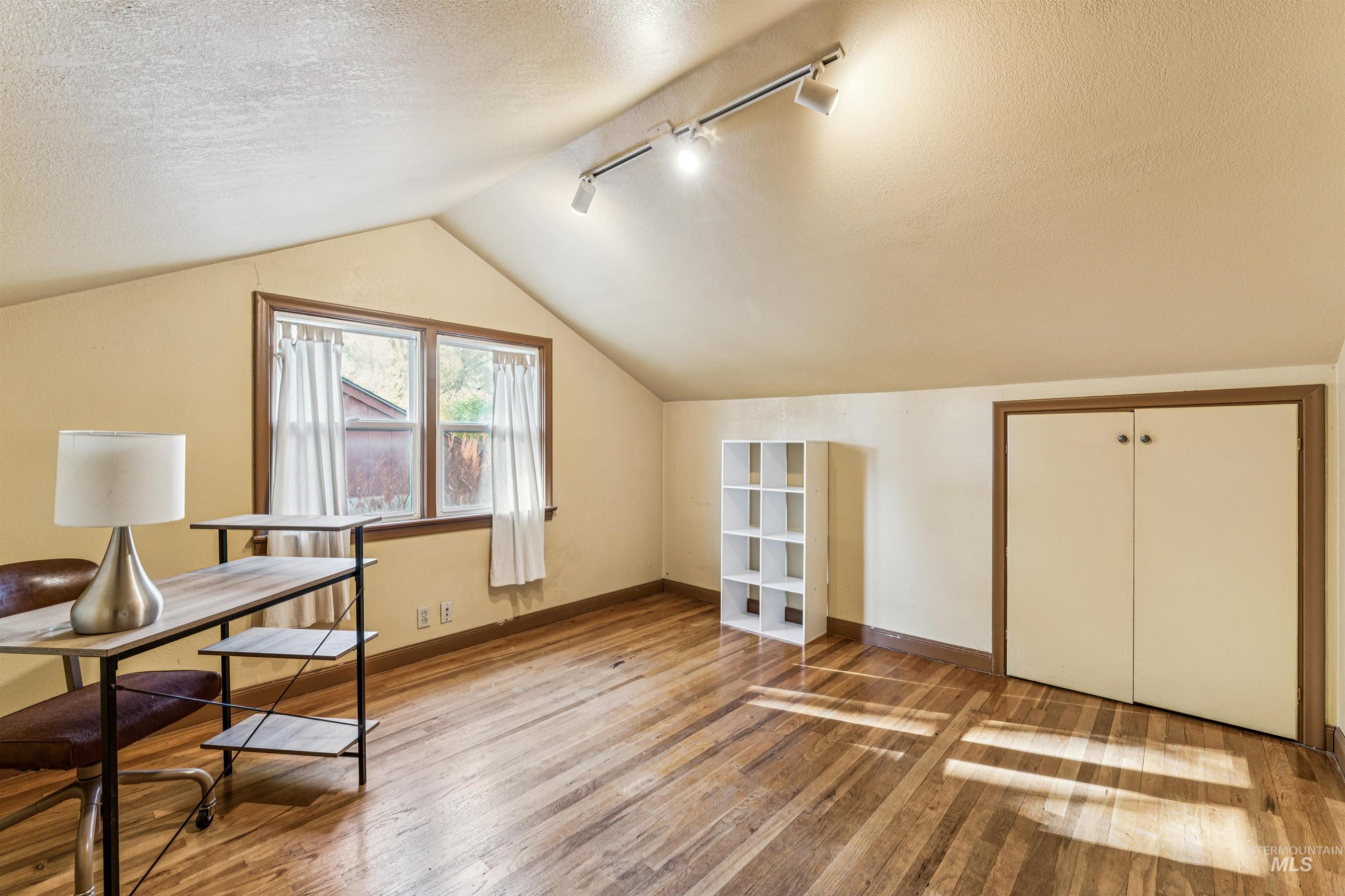 Home office with a textured ceiling, lofted ceiling, track lighting, and wood finished floors