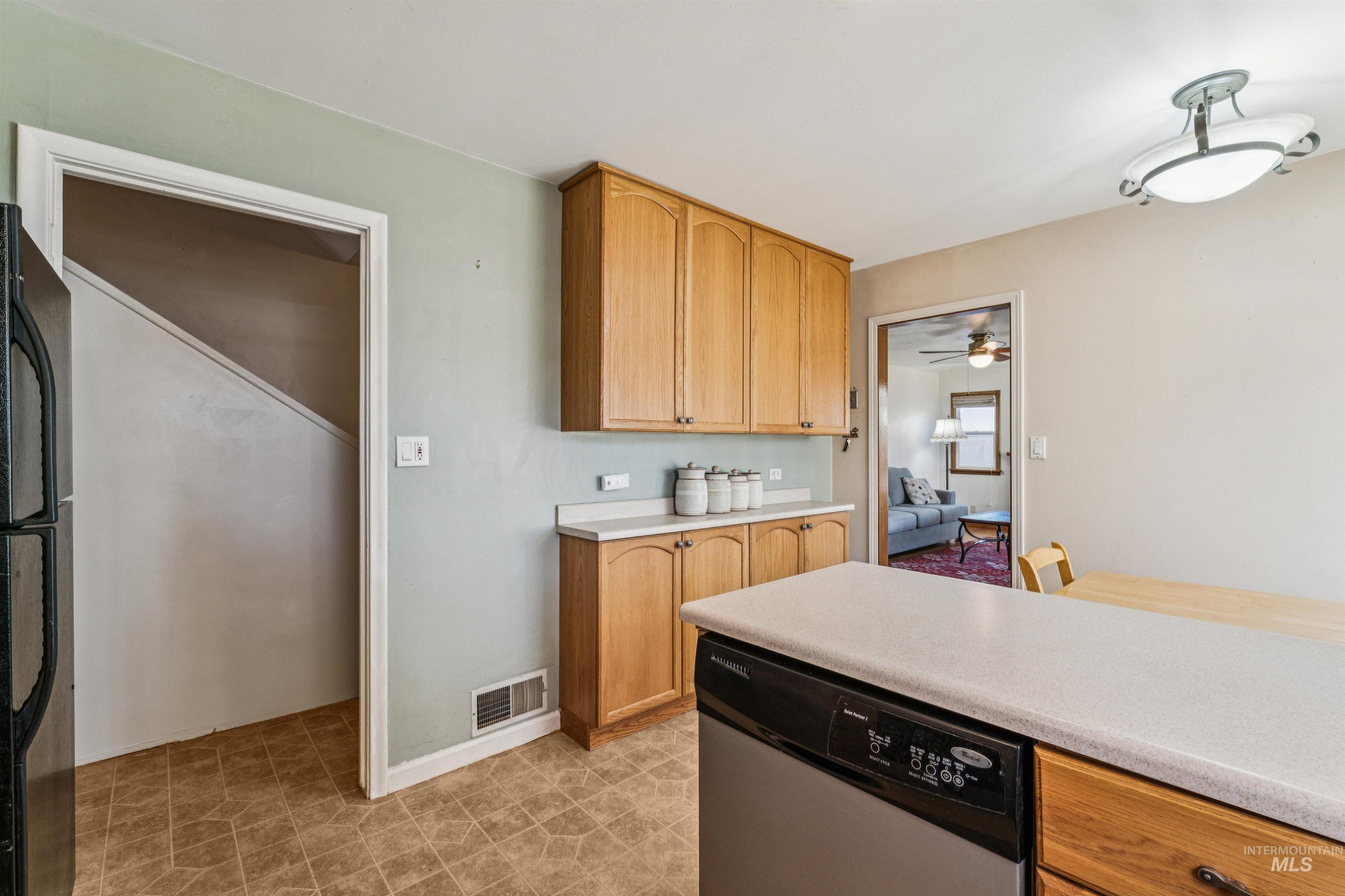 Kitchen with light countertops, stainless steel dishwasher, black refrigerator, and light brown cabinetry