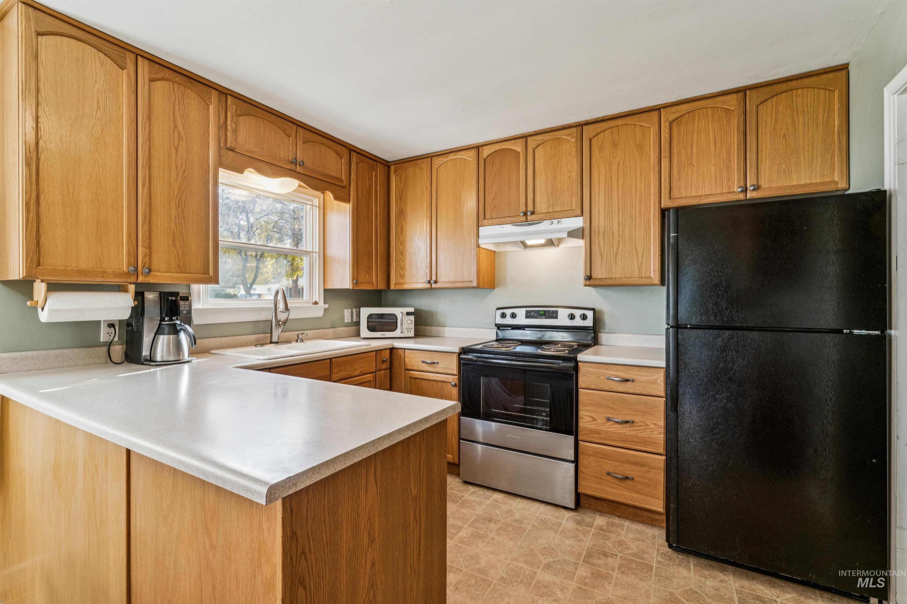 Kitchen with freestanding refrigerator, electric range, light countertops, and a peninsula