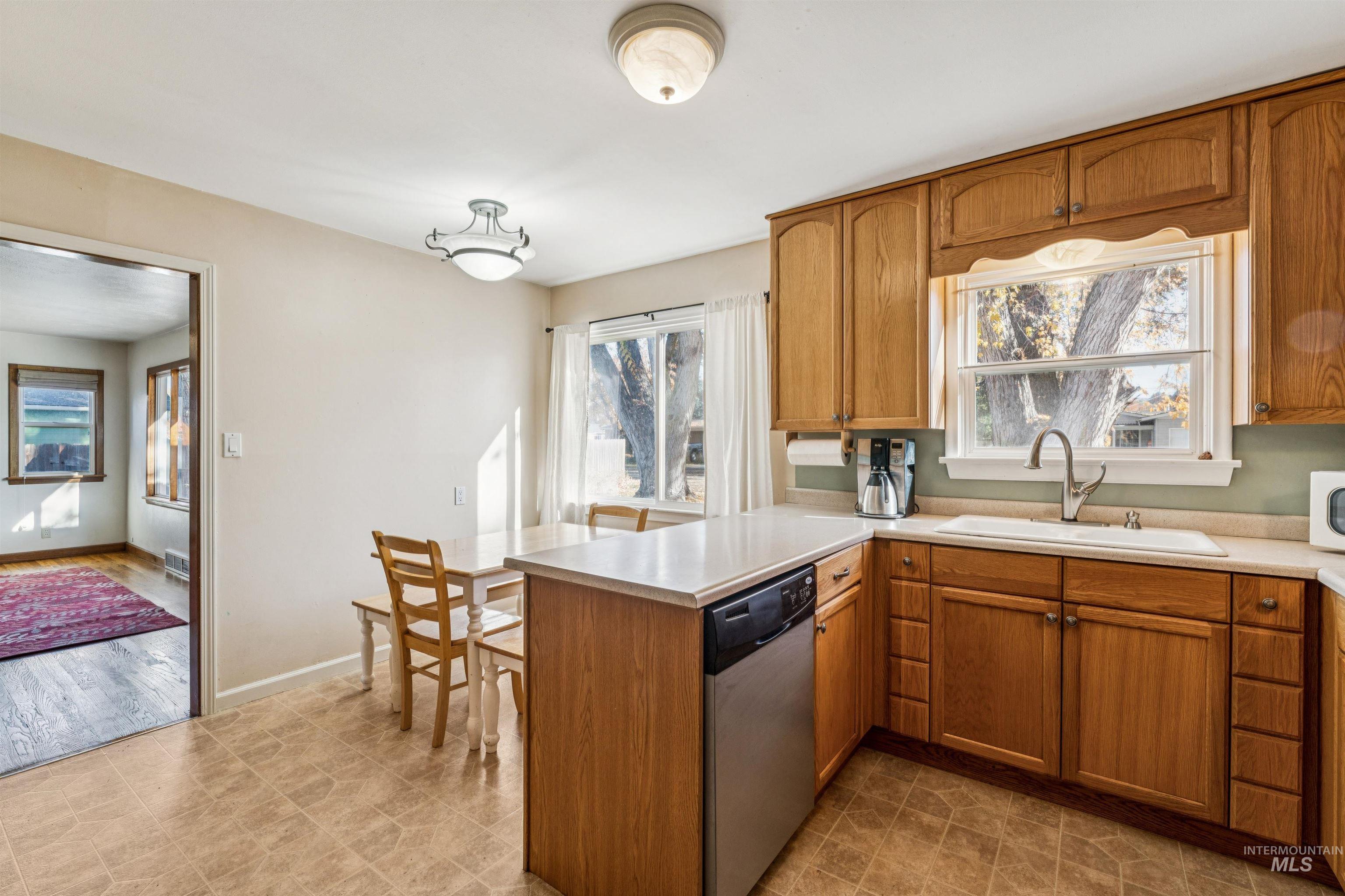 Kitchen featuring brown cabinetry, light countertops, stainless steel dishwasher, and a peninsula