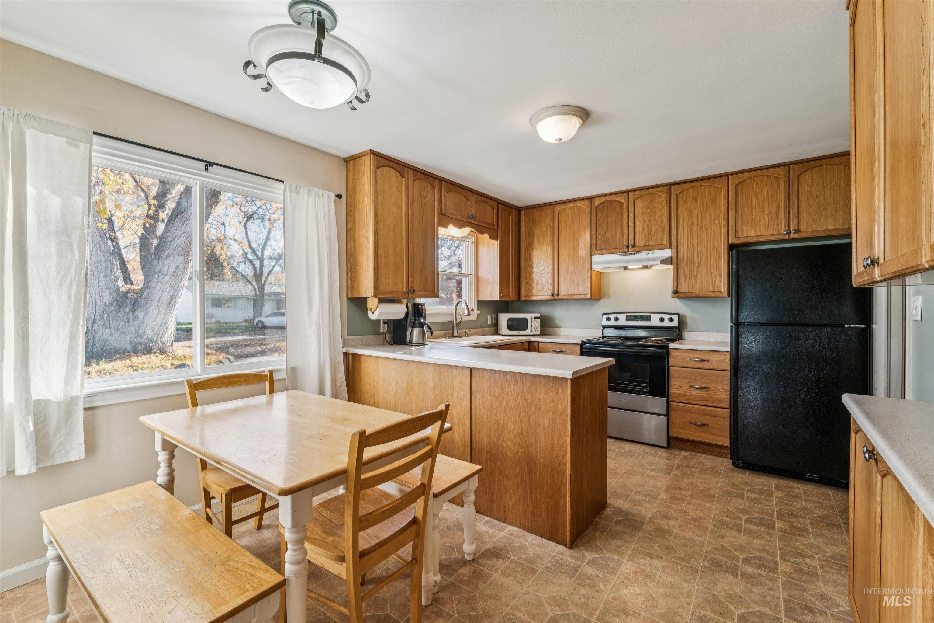 Kitchen with light countertops, freestanding refrigerator, stainless steel electric range oven, a peninsula, and healthy amount of natural light