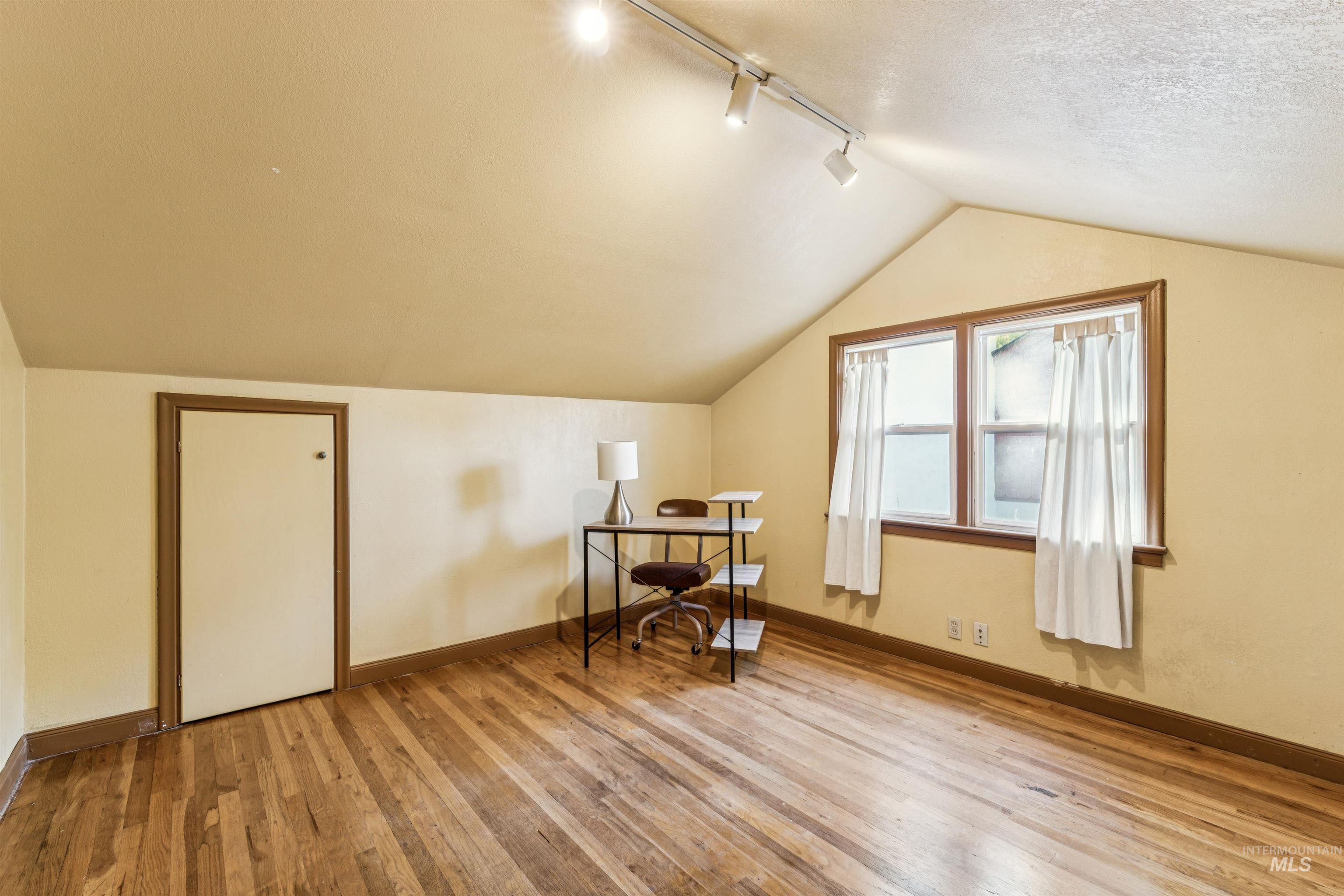 Additional living space featuring light wood-style flooring, vaulted ceiling, and a desk