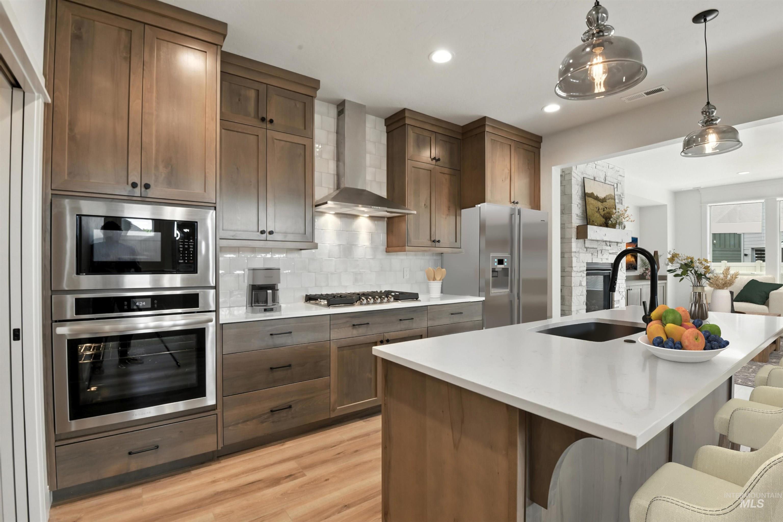 Kitchen with appliances with stainless steel finishes, wall chimney range hood, tasteful backsplash, light wood-type flooring, and light countertops