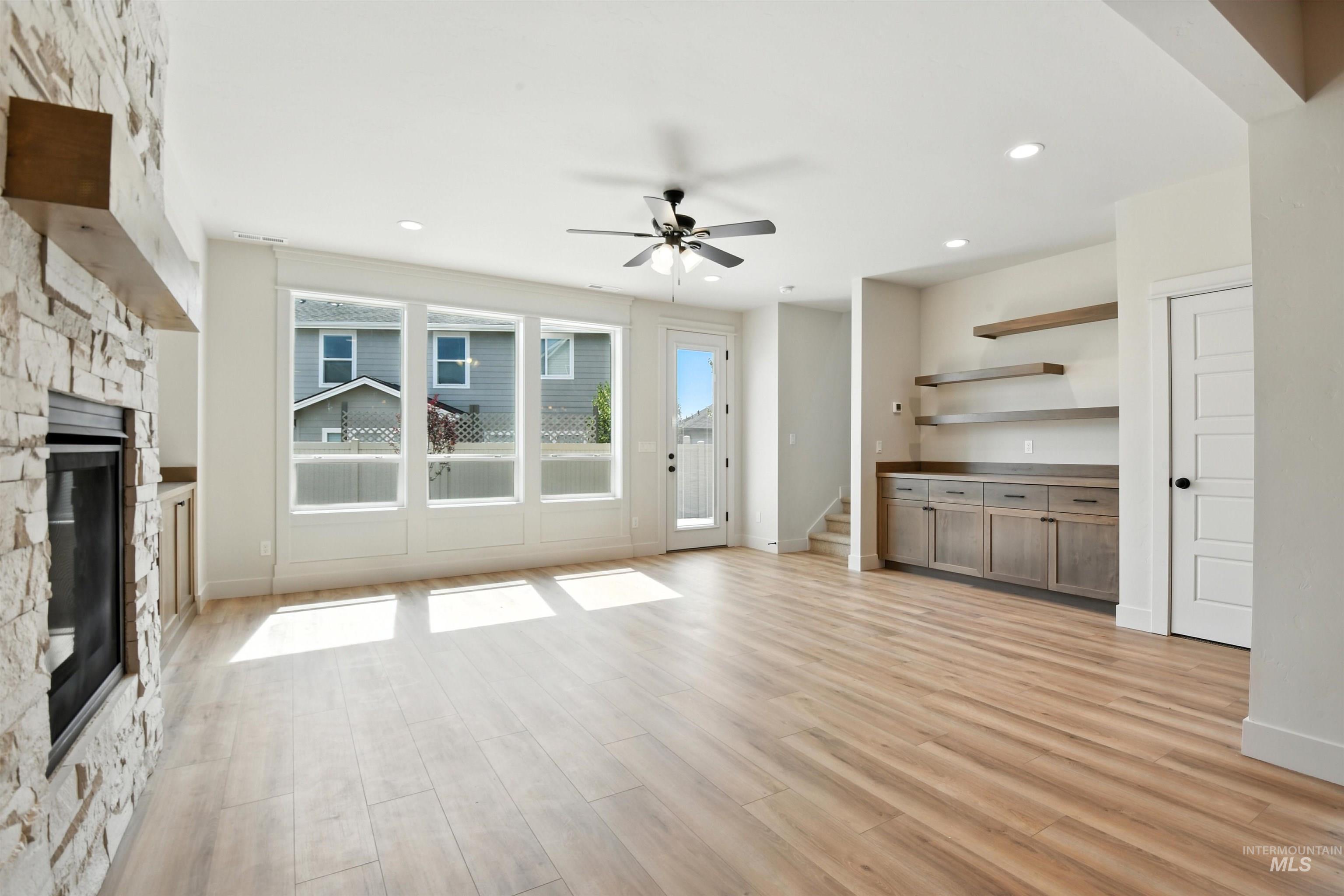 Unfurnished living room with a stone fireplace, a ceiling fan, light wood-style flooring, stairway, and recessed lighting