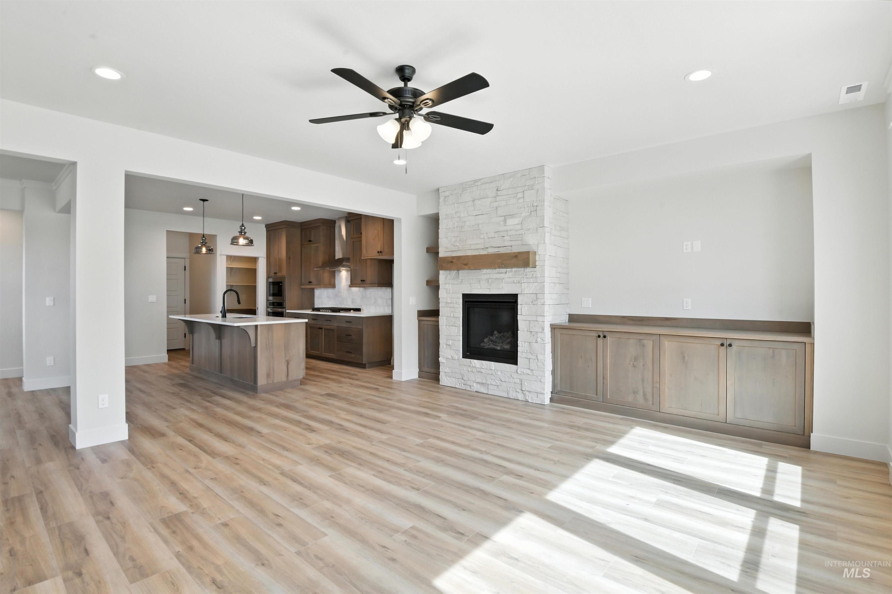 Unfurnished living room featuring ceiling fan, a fireplace, light wood-style flooring, and recessed lighting