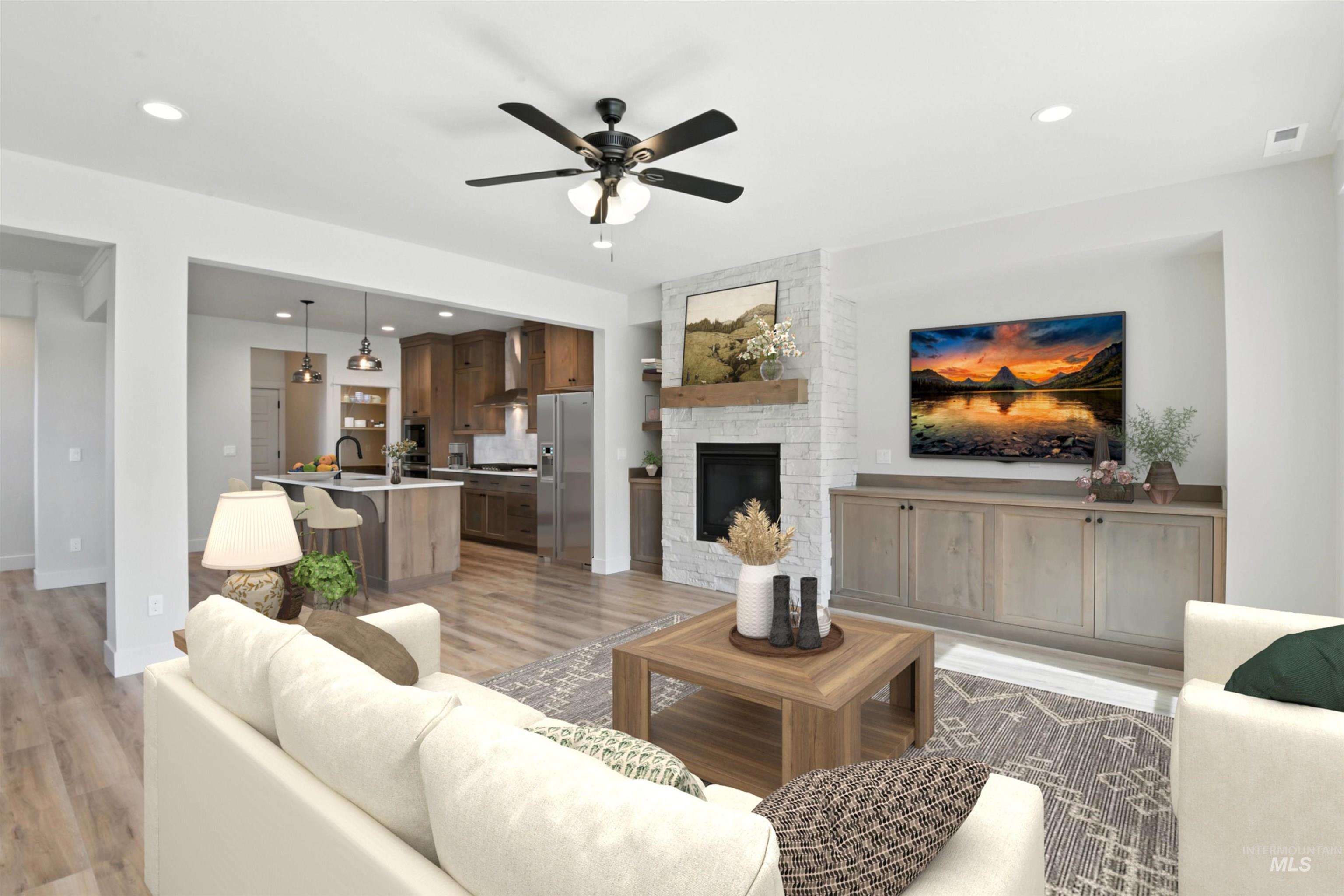 Living area with light wood-type flooring, ceiling fan, a stone fireplace, and recessed lighting