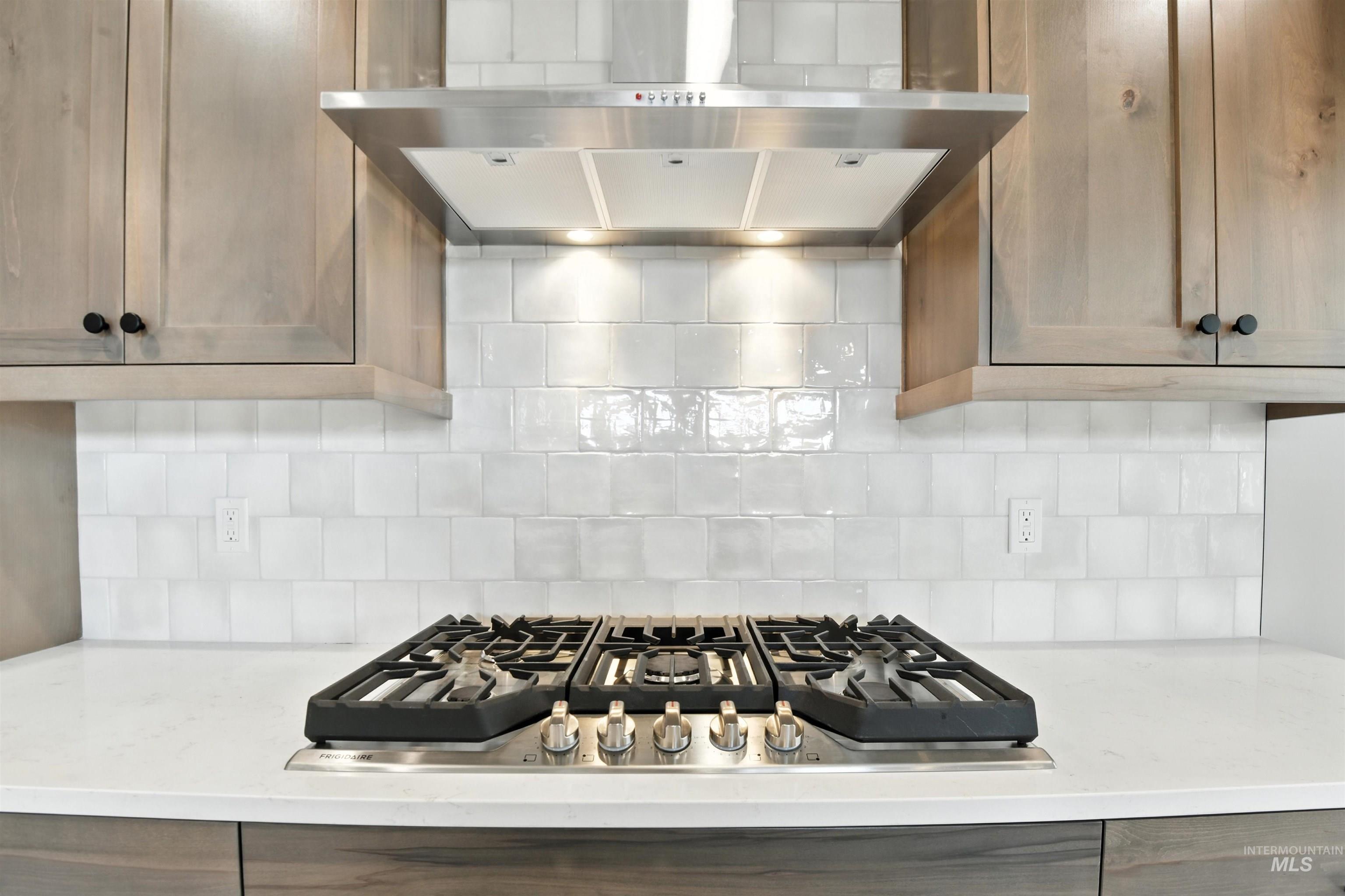 Kitchen with ventilation hood, stainless steel gas stovetop, and backsplash