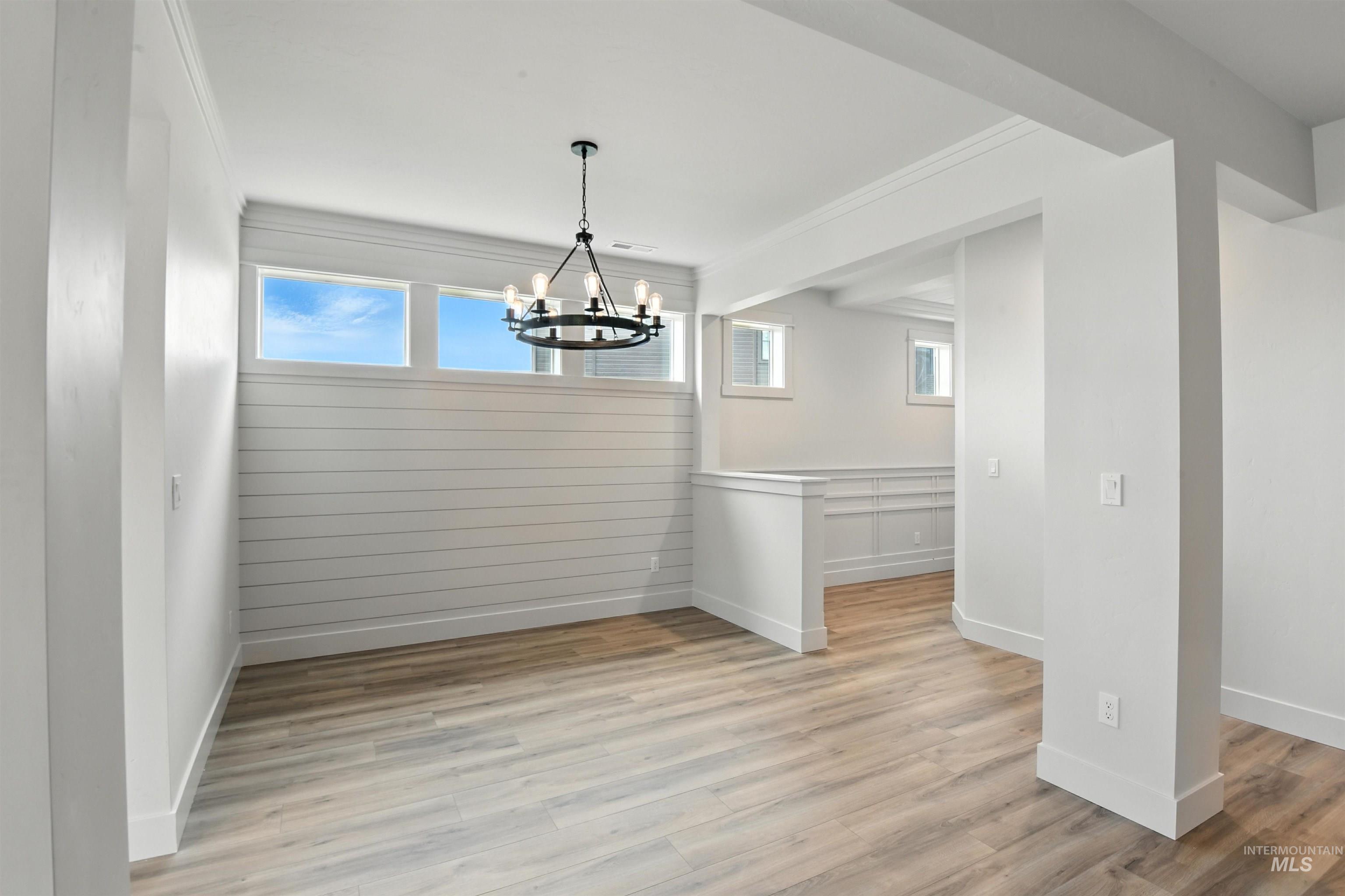Unfurnished dining area with a chandelier, light wood-style floors, and ornamental molding