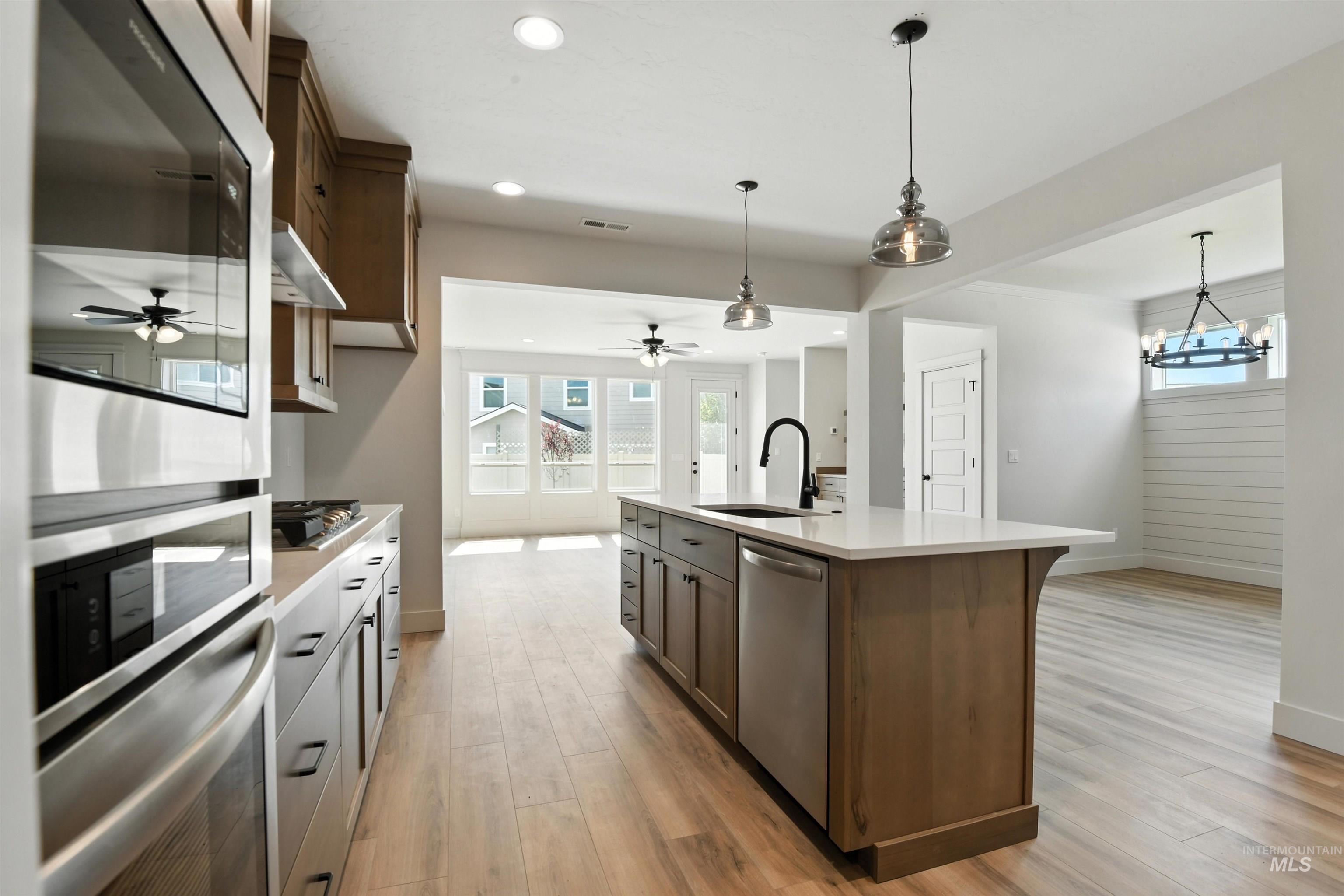Kitchen featuring appliances with stainless steel finishes, a ceiling fan, light countertops, an island with sink, and recessed lighting