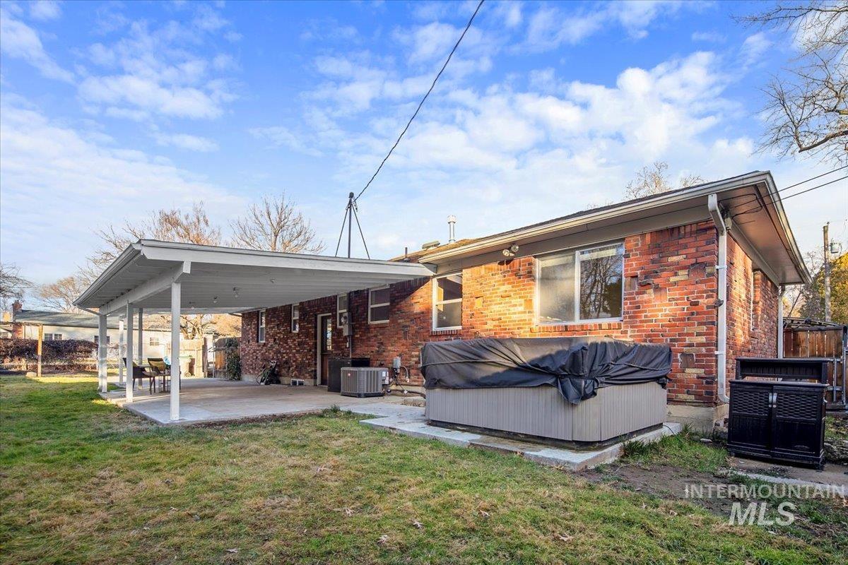 Rear view of property with a hot tub, a patio area, a lawn, and brick siding