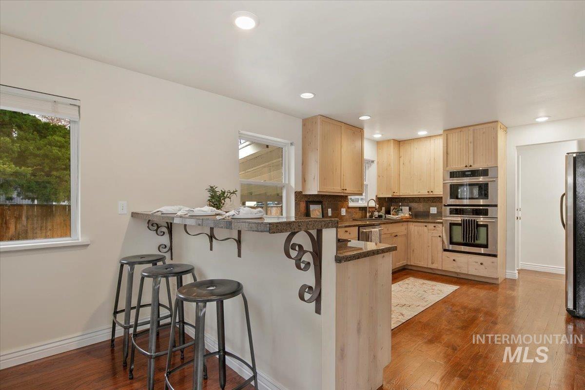Kitchen featuring light brown cabinets, a kitchen bar, dark wood-type flooring, and appliances with stainless steel finishes