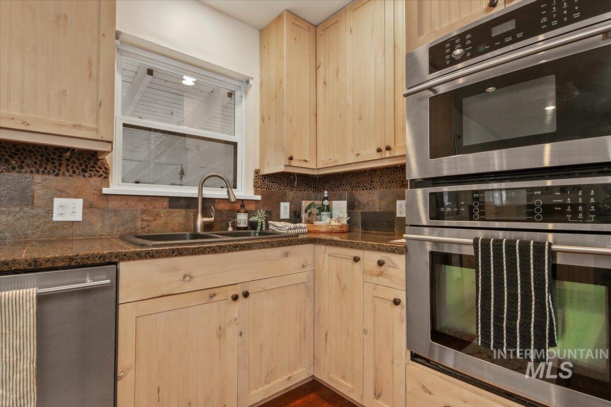 Kitchen with stainless steel appliances, light brown cabinetry, backsplash, and dark wood-style flooring