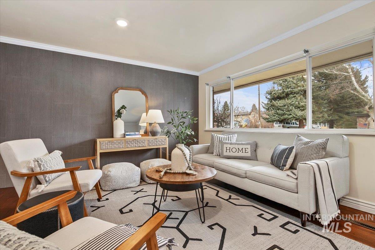 Living room with an accent wall, wallpapered walls, wood finished floors, and crown molding