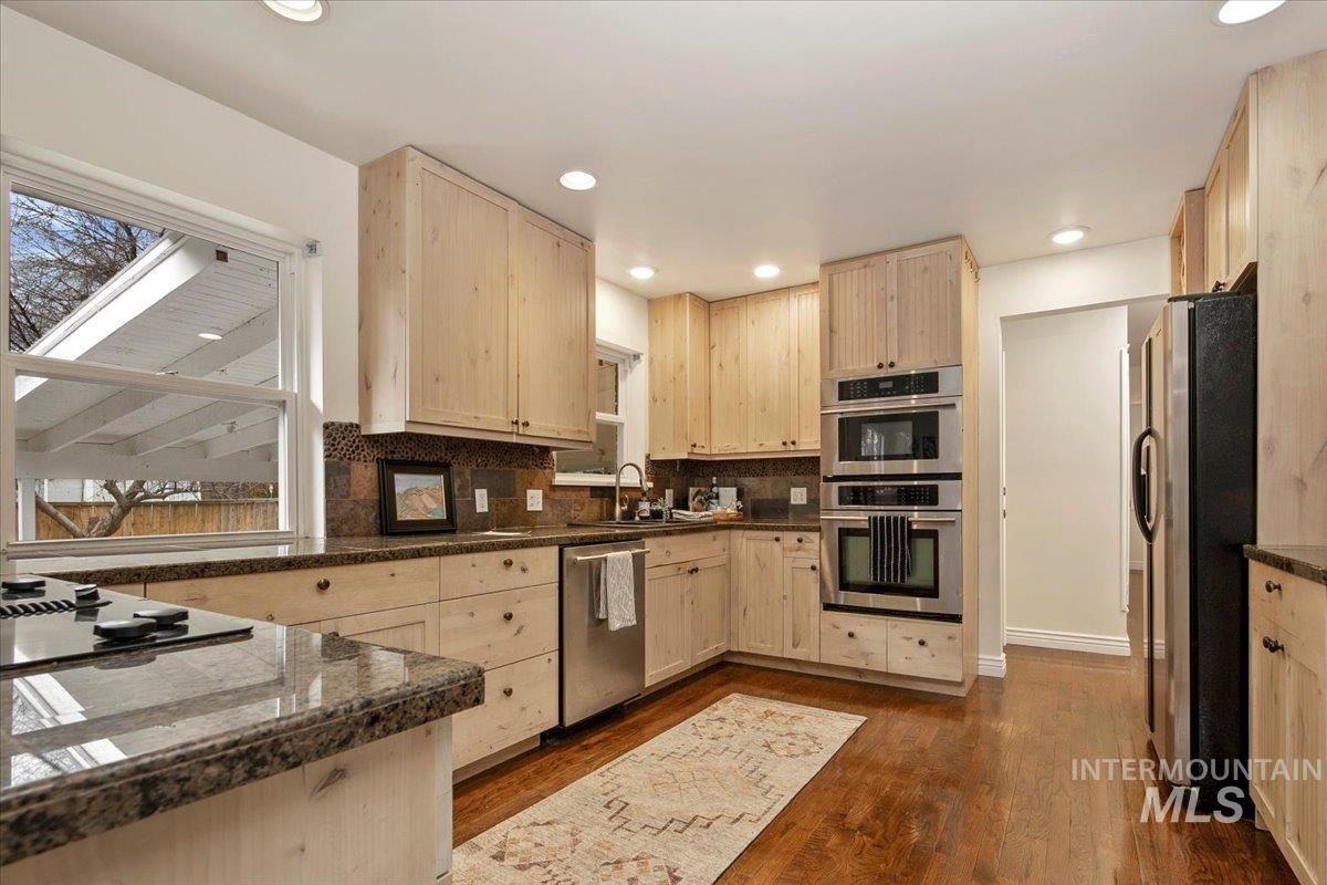 Kitchen with light brown cabinets, stainless steel appliances, dark wood finished floors, backsplash, and recessed lighting