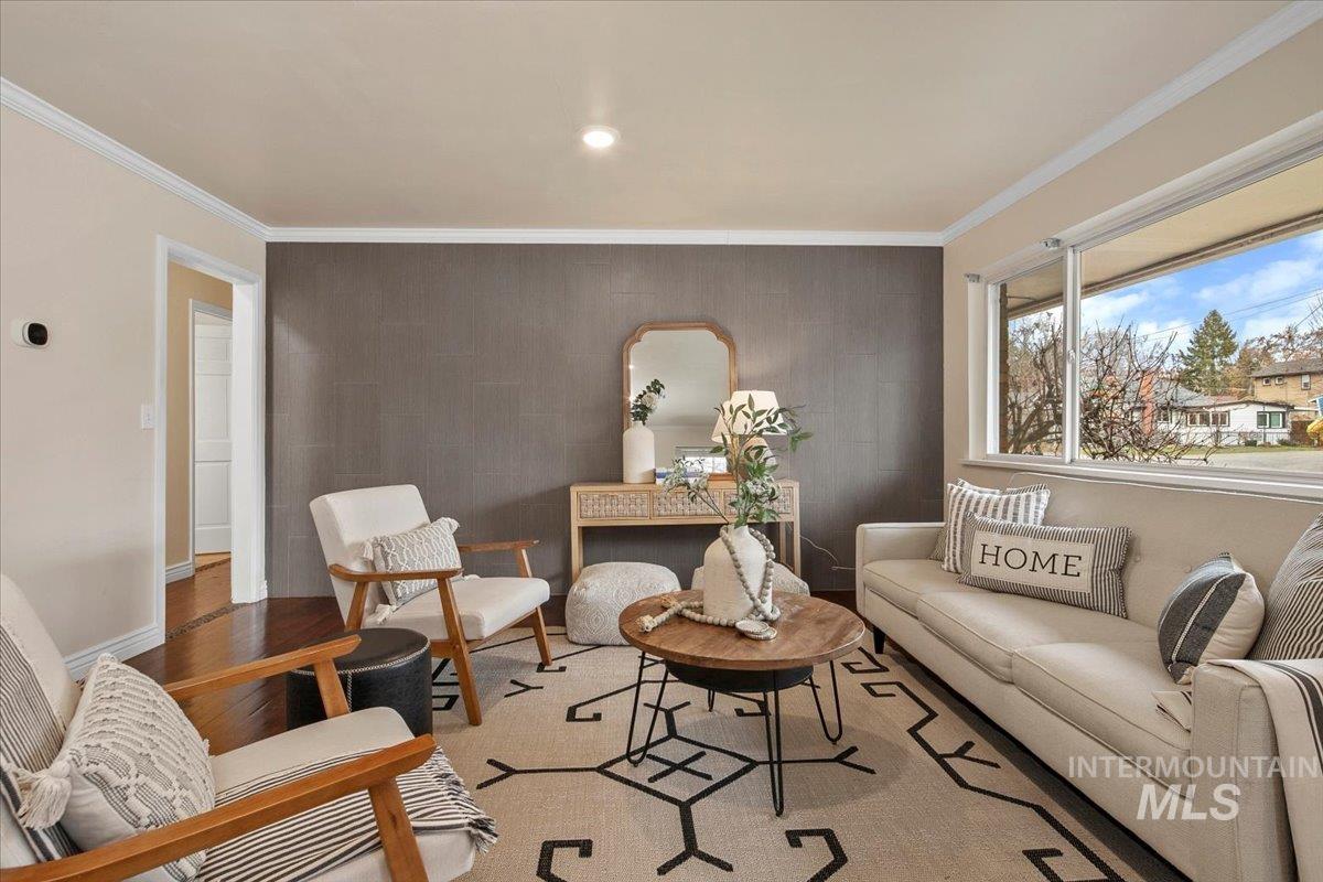 Living area with an accent wall, crown molding, wood finished floors, and recessed lighting